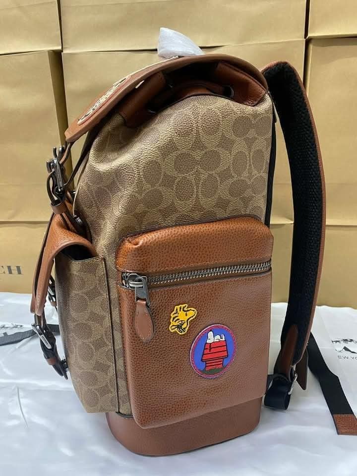 Coach Snoopy Patchwork Backpack (Category: Luxury Bags & Wallets) located in Manila. Submitted by santosrich_419 (Listing ID 1416998724, Image 2). Description: Coach backpack features a brown leather and signature canvas design with Snoopy patches. It has multiple pockets, including a front zippered pocket and side pockets. The backpack has adjustable straps and a drawstring closure. Dimensions are approximately 42x30cm..