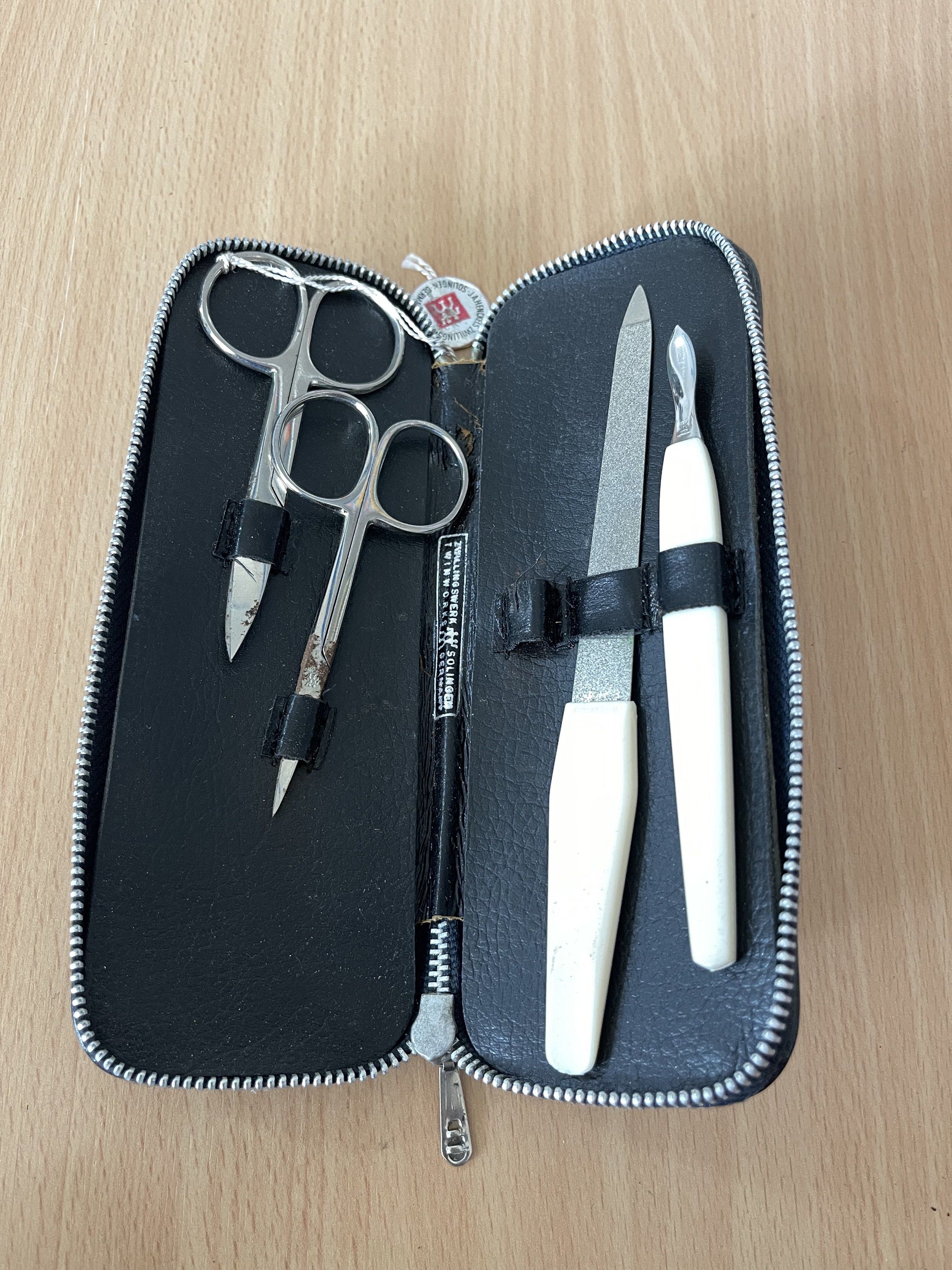 Manicure set (Category: Hands & Nails) located in San Fernando. Submitted by japansurpluselyu (Listing ID 1417022416, Image 1). Description: 1. *Small stainless steel scissors* with black handle grips, positioned on the left side of the pouch. 2. *A pointed nail file or push tool* with a black handle and white tip, placed next to the scissors. 3. *A metal nail clipper* with a white handle, secured in an elastic strap on the right side of the pouc