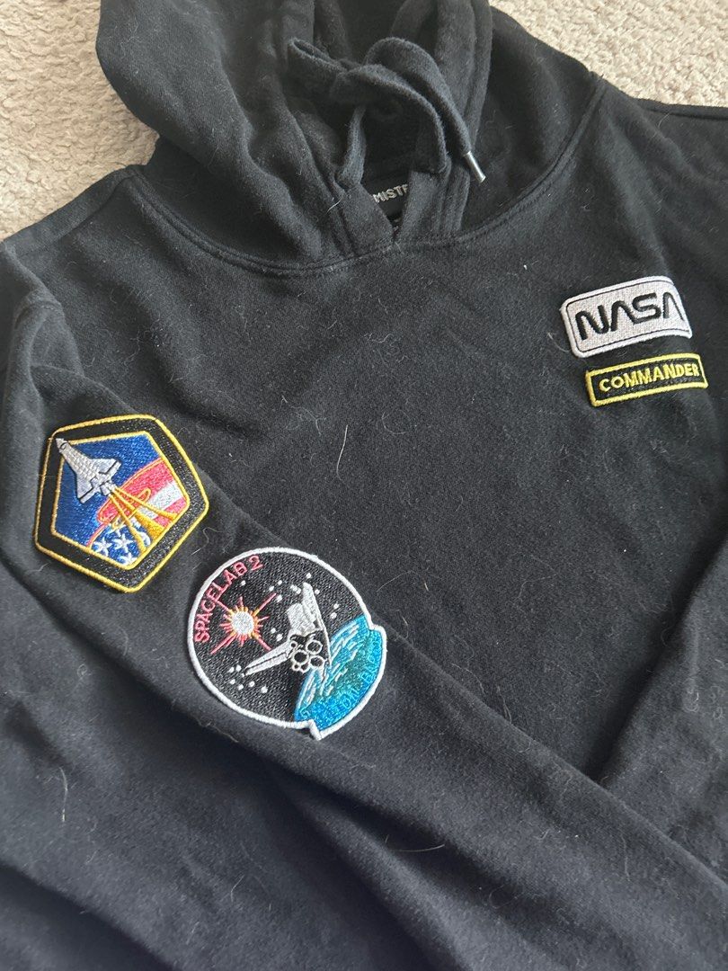 NASA Cropped Hoodie (Category: Coats, Jackets and Outerwear) located in Taguig. Submitted by rcdeclutter (Listing ID 1416907003, Image 2). Description: - Black cropped hoodie - NASA patches on front and left sleeve - Drawstring hood - Long sleeves - Includes NASA logo and "Commander" patches - Space-themed designs - Cut bottom hem.
