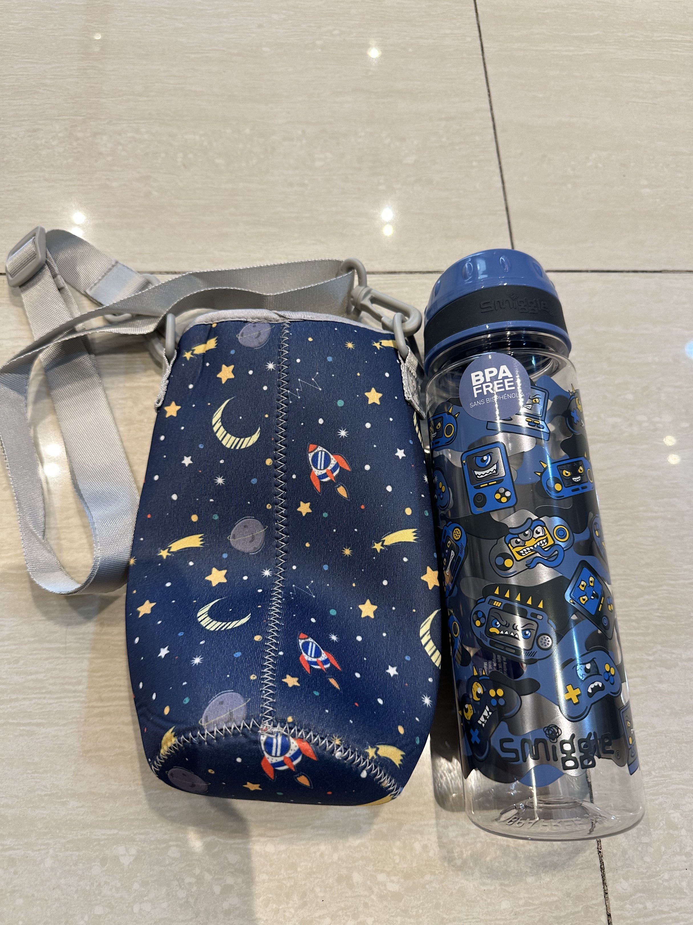 Smiggle Water Bottle with Sleeve (Category: Water Bottles & Tumblers) located in Singapore. Submitted by lynnzi80 (Listing ID 1416922284, Image 1). Description: Smiggle water bottle with a matching sleeve. The bottle is BPA-free and features a fun gaming design. The sleeve has a space-themed pattern and a strap for easy carrying. Perfect for school or outdoor activities..