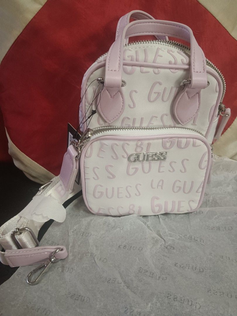 Guess Mini Handbag with Shoulder Strap (Category: Shoulder Bags) located in Caloocan City. Submitted by jee2727 (Listing ID 1417218728, Image 2). Description: - Brand new Guess mini handbag - Color: White and Pink - Features the iconic Guess logo - Includes a top handle and a detachable shoulder strap - Has a front pocket and a main zippered compartment - Comes with original tags attached.