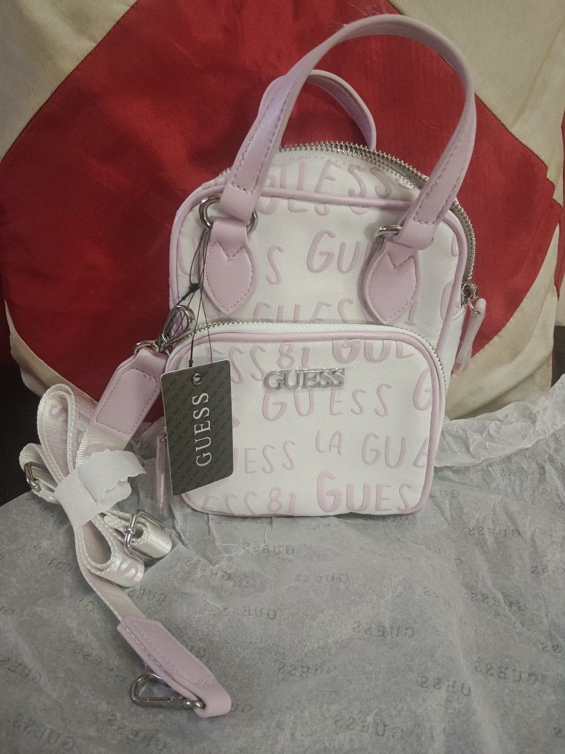 Guess Mini Handbag with Shoulder Strap (Category: Shoulder Bags) located in Caloocan City. Submitted by jee2727 (Listing ID 1417218728, Image 1). Description: - Brand new Guess mini handbag - Color: White and Pink - Features the iconic Guess logo - Includes a top handle and a detachable shoulder strap - Has a front pocket and a main zippered compartment - Comes with original tags attached.