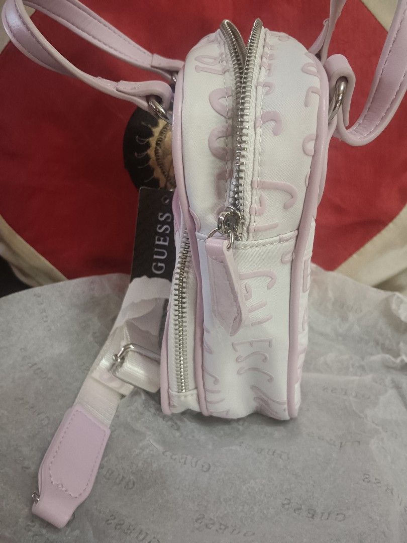 Guess Mini Handbag with Shoulder Strap (Category: Shoulder Bags) located in Caloocan City. Submitted by jee2727 (Listing ID 1417218728, Image 3). Description: - Brand new Guess mini handbag - Color: White and Pink - Features the iconic Guess logo - Includes a top handle and a detachable shoulder strap - Has a front pocket and a main zippered compartment - Comes with original tags attached.