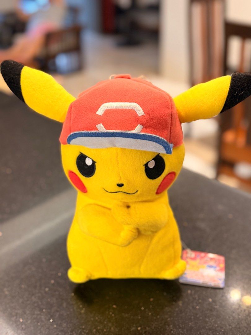 Pokemon Pikachu Plush Ash Cap (Category: Plushies & Soft Toys) located in Paranaque City. Submitted by thirdys_locker (Listing ID 1417314797, Image 2). Description: - Authentic Pikachu plush toy - Features a red cap with white and blue brim - Approximately 25cm tall - Includes Crane King and Banpresto tag - Tag features Pikachu and Ash - Yellow plush with black ears and red cheeks.