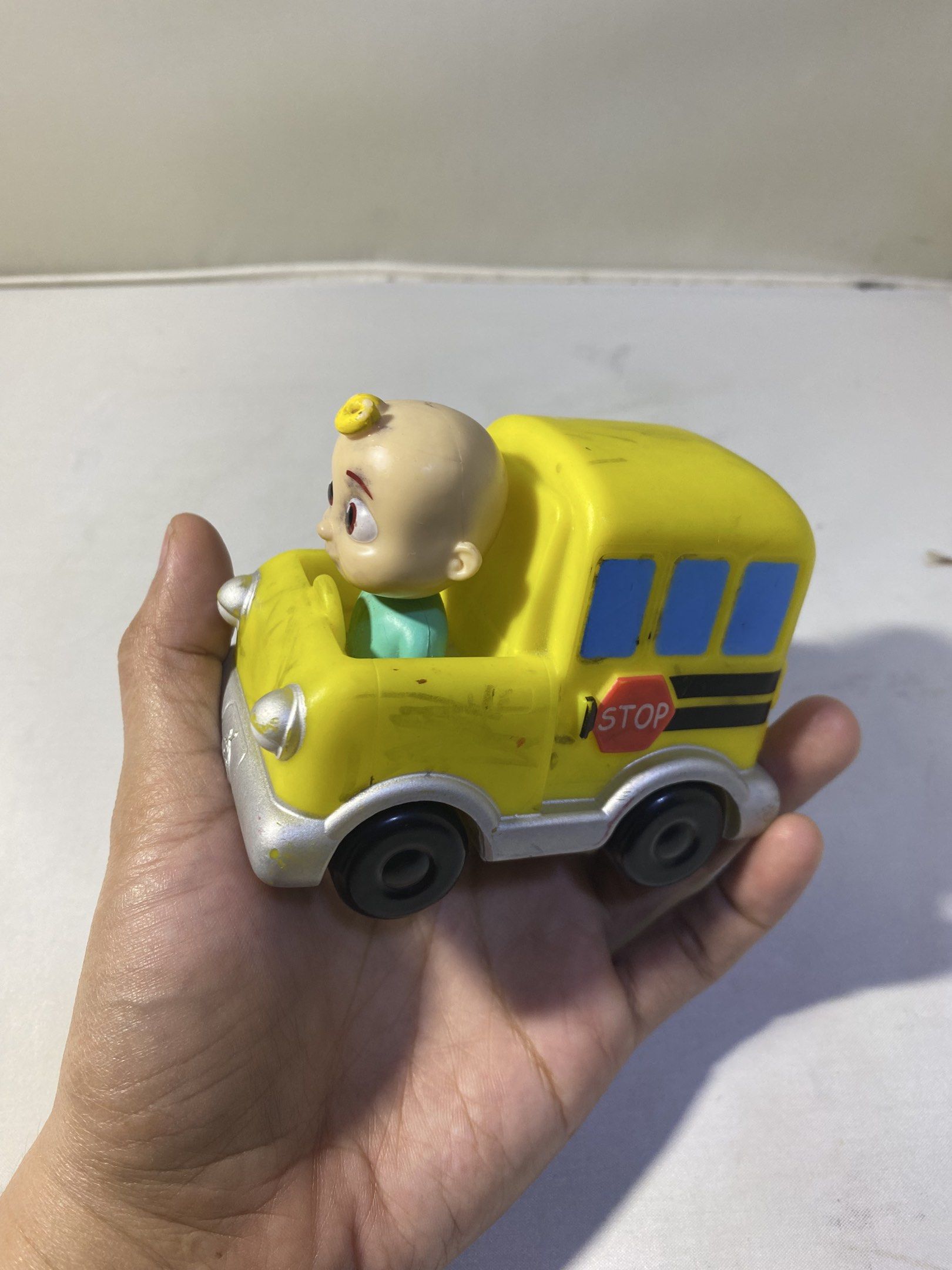 CoComelon School Bus Toy (Category: Kids Toys) located in Pasacao. Submitted by wengpullar37205 (Listing ID 1417699070, Image 3). Description: CoComelon school bus toy featuring a CoComelon character. The bus is yellow with blue windows and a stop sign. The toy has black wheels and a silver base. The character is seated inside the bus. The bottom of the toy has the manufacturer's information..