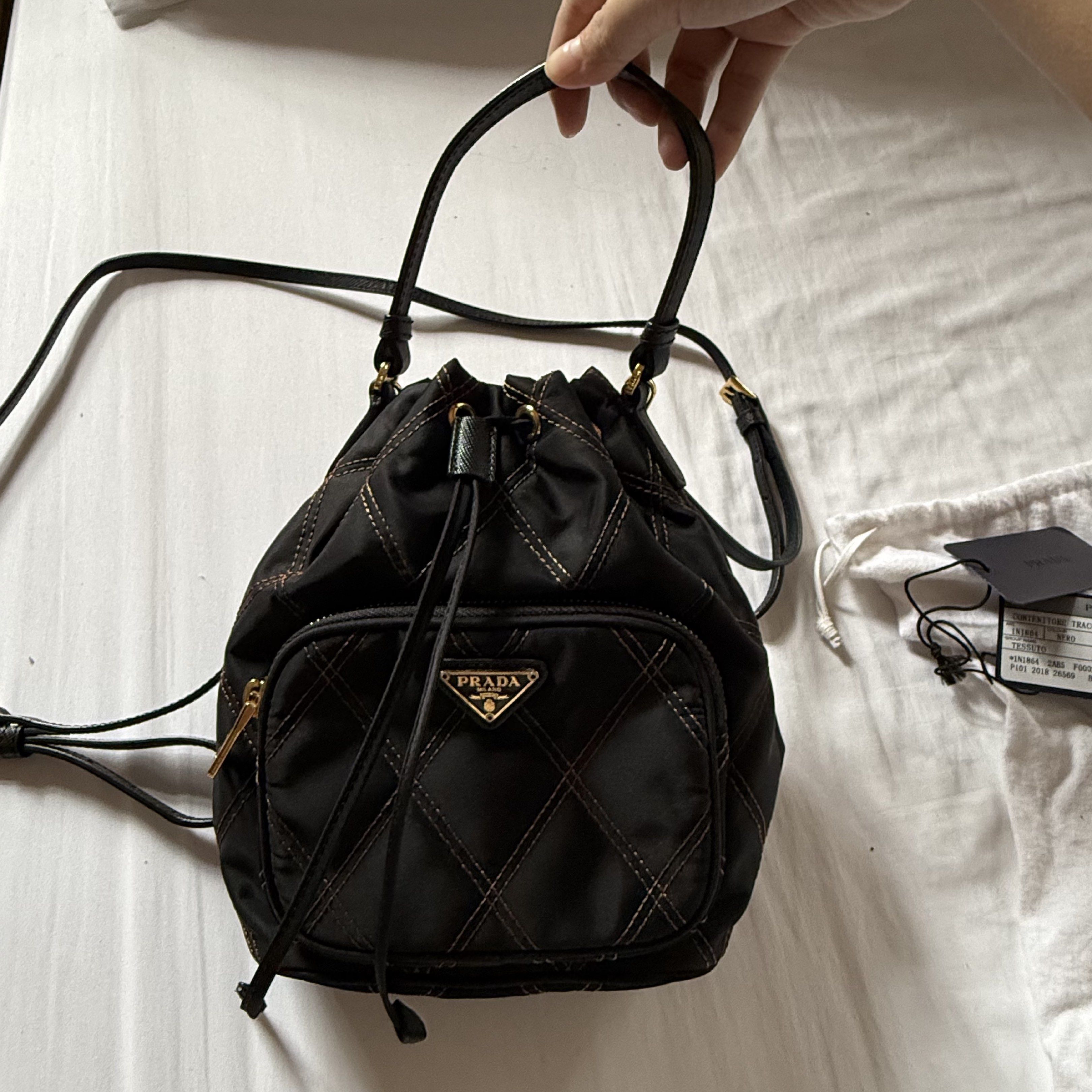 Prada Quilted Nylon Bucket Bag (Category: Luxury Bags & Wallets) located in Quezon City. Submitted by aligatsss (Listing ID 1417615498, Image 2). Description: - NGA Prada bucket bag - Black nylon with gold-tone hardware - Drawstring closure - Front pocket with Prada logo - Detachable shoulder strap - Includes authenticity cards and dust bag - Interior features Prada Milano logo - Quilted design with gold stitching.