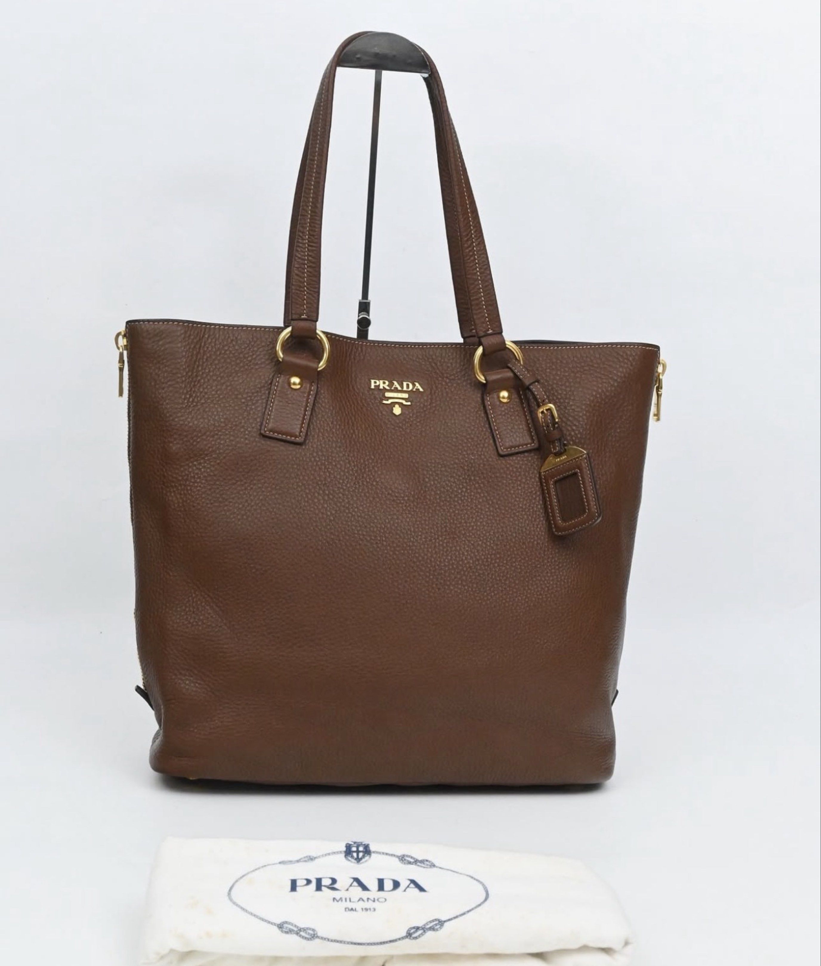 AUTHENTIC Prada Brown Leather Tote Bag (Category: Luxury Bags & Wallets) located in Manila. Submitted by itsmecamieeee (Listing ID 1417988117, Image 1). Description: - Authentic Prada tote bag - Brown leather exterior (Smooth and no cracks) - Gold-tone hardware (Hardware still goldish) - Zip closure (Still goldish) - Structured shape with flat base - Prada-branded interior lining - Detachable leather tag - Includes dust bag - No flaws - Negotiabl