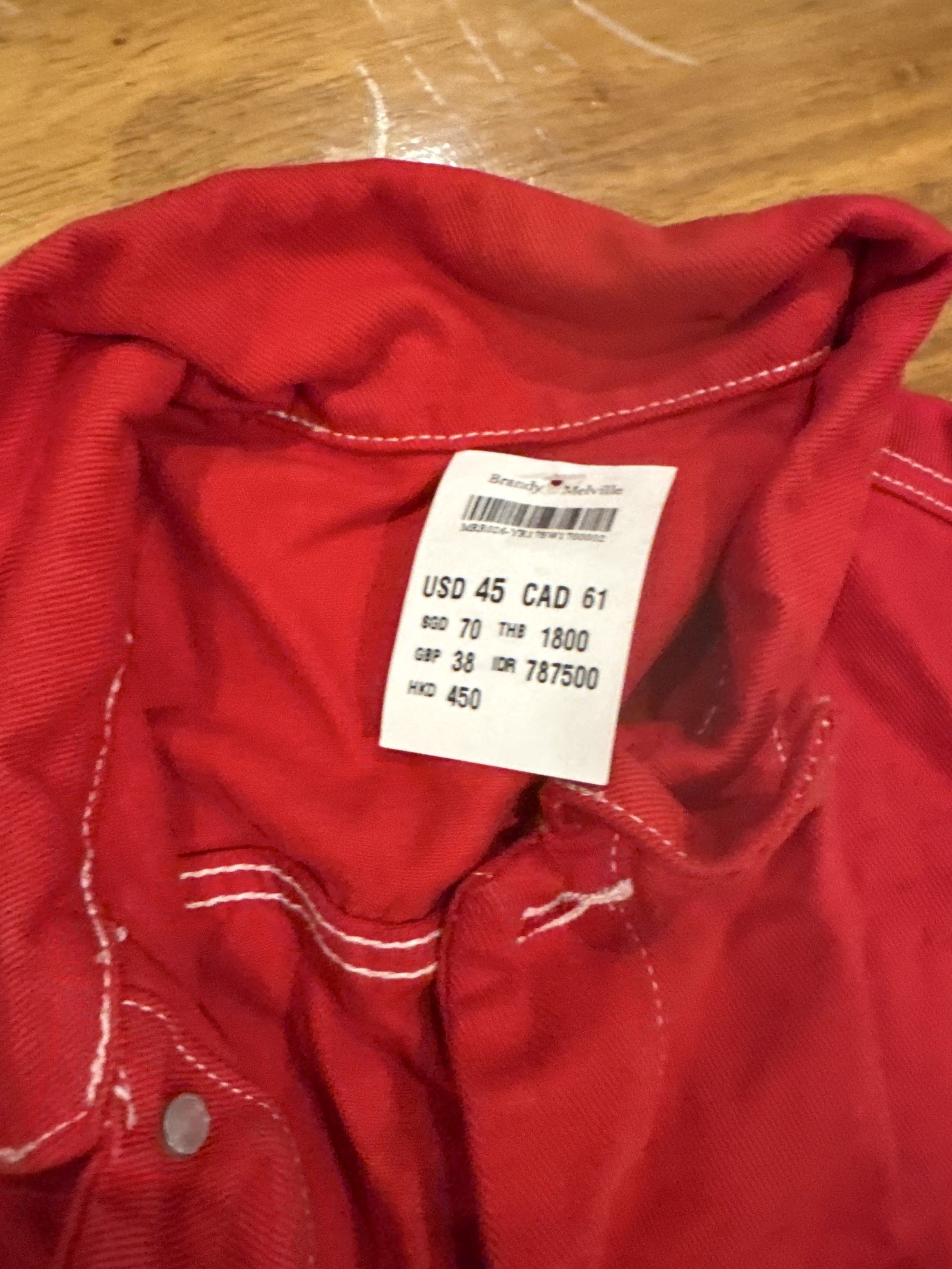 Brandy Melville Red Jacket (Category: Coats, Jackets and Outerwear) located in Manila. Submitted by eb.declutters (Listing ID 1417957560, Image 2). Description: - Brandy Melville red jacket - Button-up front - Two chest pockets - White stitching details - Collared neckline - Long sleeves - Original price tag with USD, CAD, GBP, THB, IDR, and HKD prices.