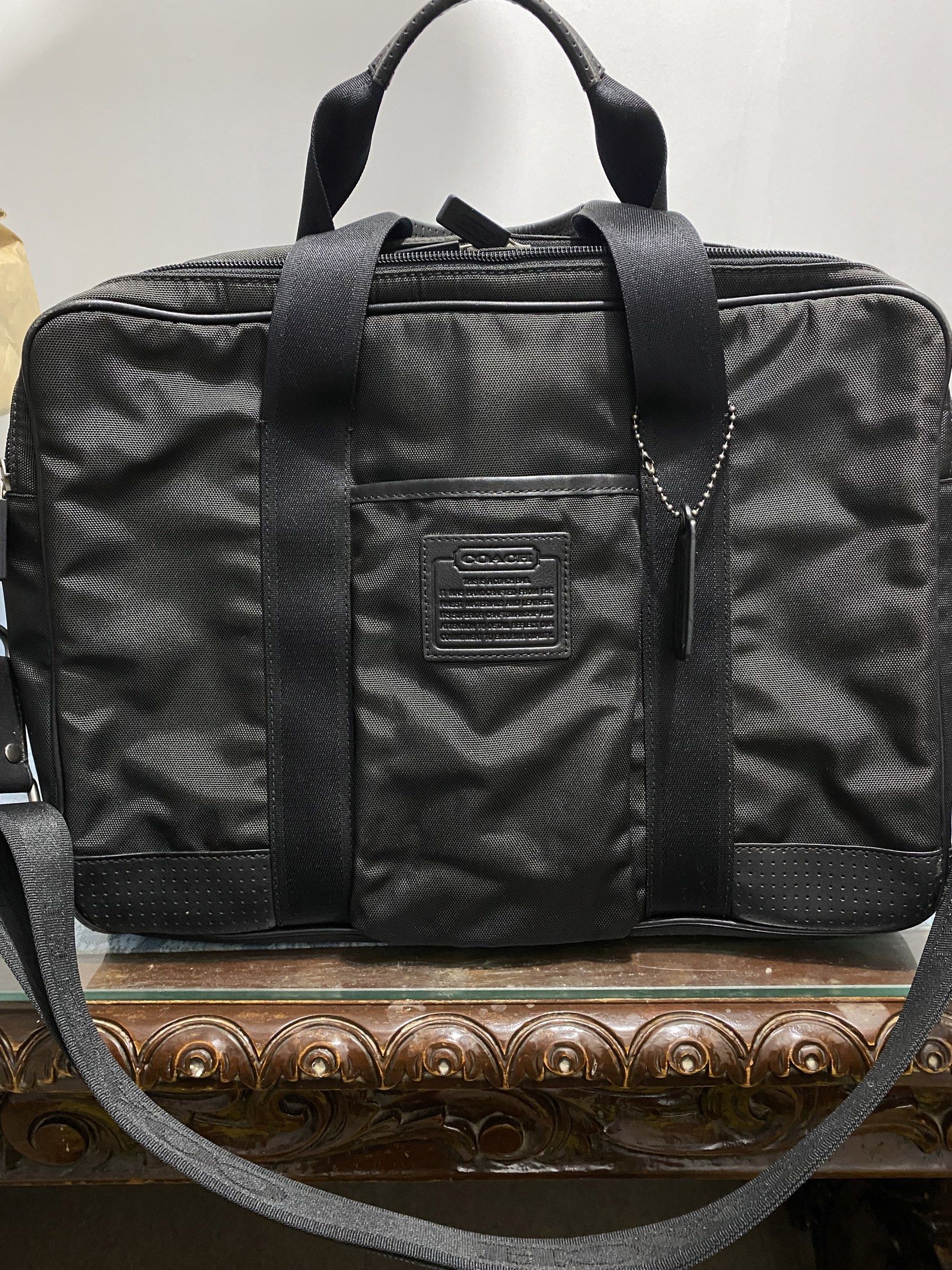 Coach Black Briefcase (Category: Briefcases) located in Cagayan de Oro. Submitted by cu_2022 (Listing ID 1417992831, Image 1). Description: Black Coach sling bag with a top handle and a detachable shoulder strap. Features a main compartment with multiple pockets and a zippered closure. Includes a Coach leather tag and a Coach logo on the front. The bag has a sleek, professional design, suitable for carrying documents and other essentials..