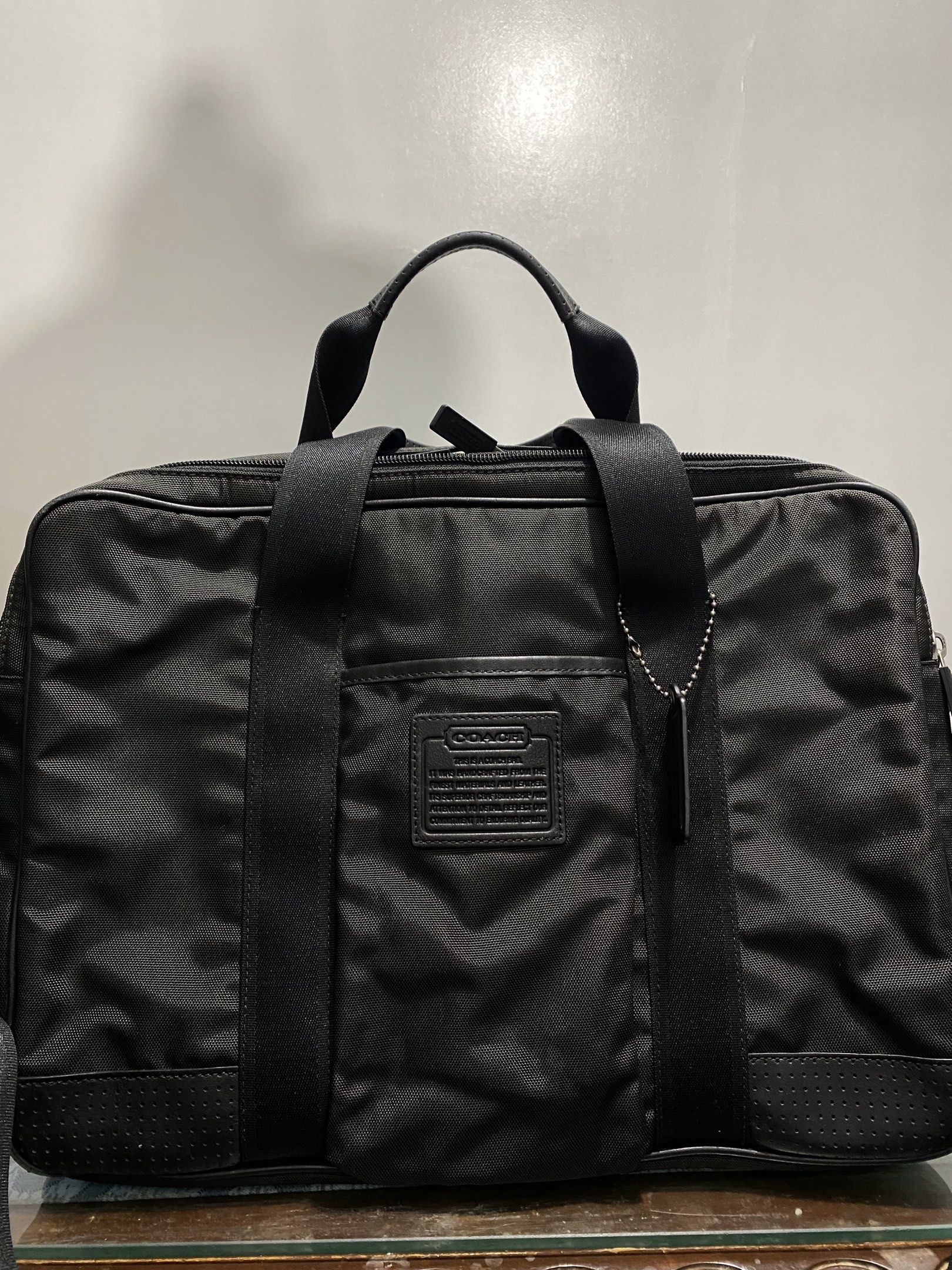 Coach Black Briefcase (Category: Briefcases) located in Cagayan de Oro. Submitted by cu_2022 (Listing ID 1417992831, Image 2). Description: Black Coach sling bag with a top handle and a detachable shoulder strap. Features a main compartment with multiple pockets and a zippered closure. Includes a Coach leather tag and a Coach logo on the front. The bag has a sleek, professional design, suitable for carrying documents and other essentials..