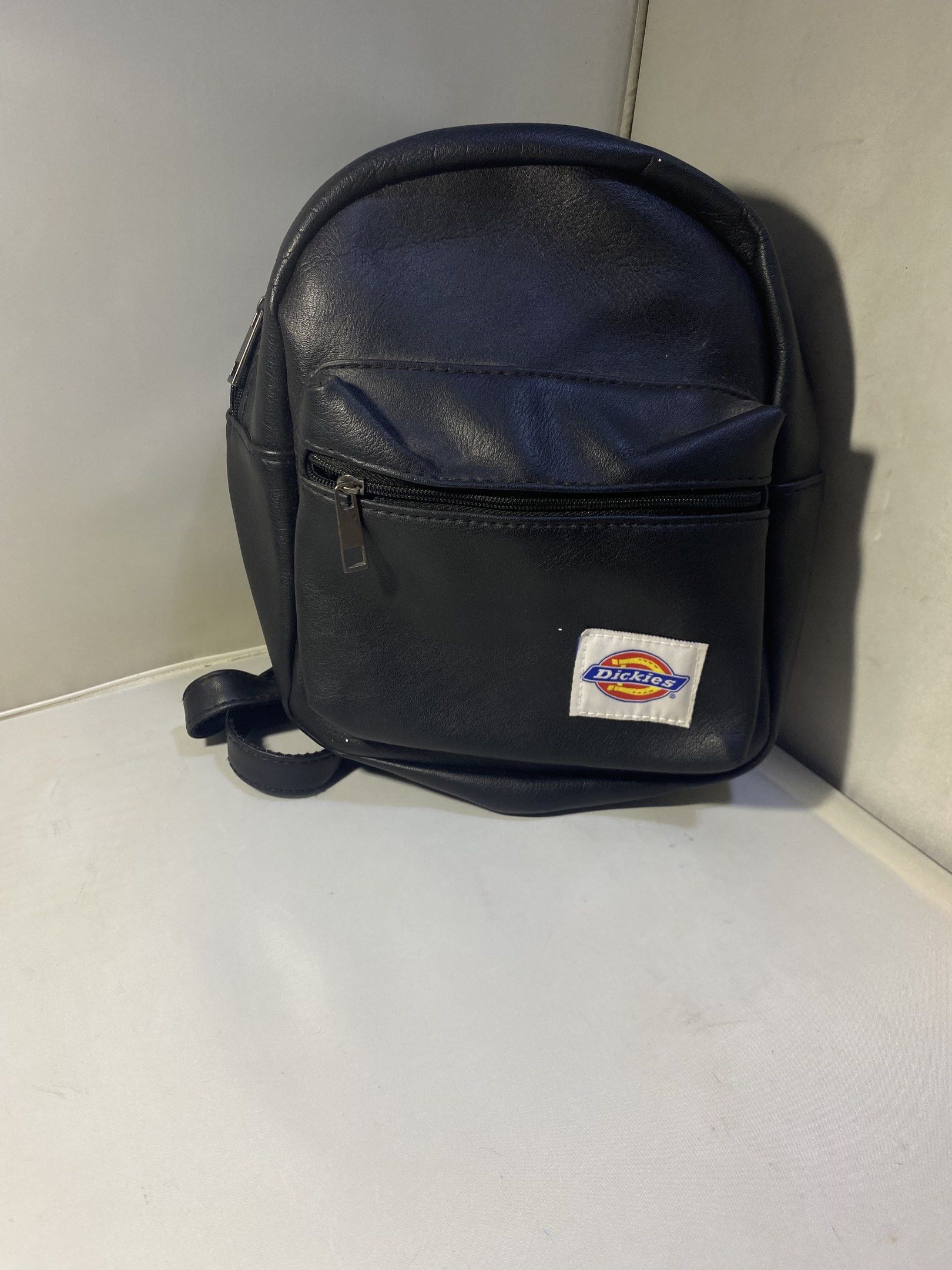Dickies Black Mini Backpack (Category: Backpacks) located in Pasacao. Submitted by wengpullar37205 (Listing ID 1417943088, Image 1). Description: Black mini backpack features a front pocket with a zipper and a Dickies logo patch. It has adjustable straps and a top handle. The main compartment has a zipper closure. It's a compact size, suitable for carrying essentials..