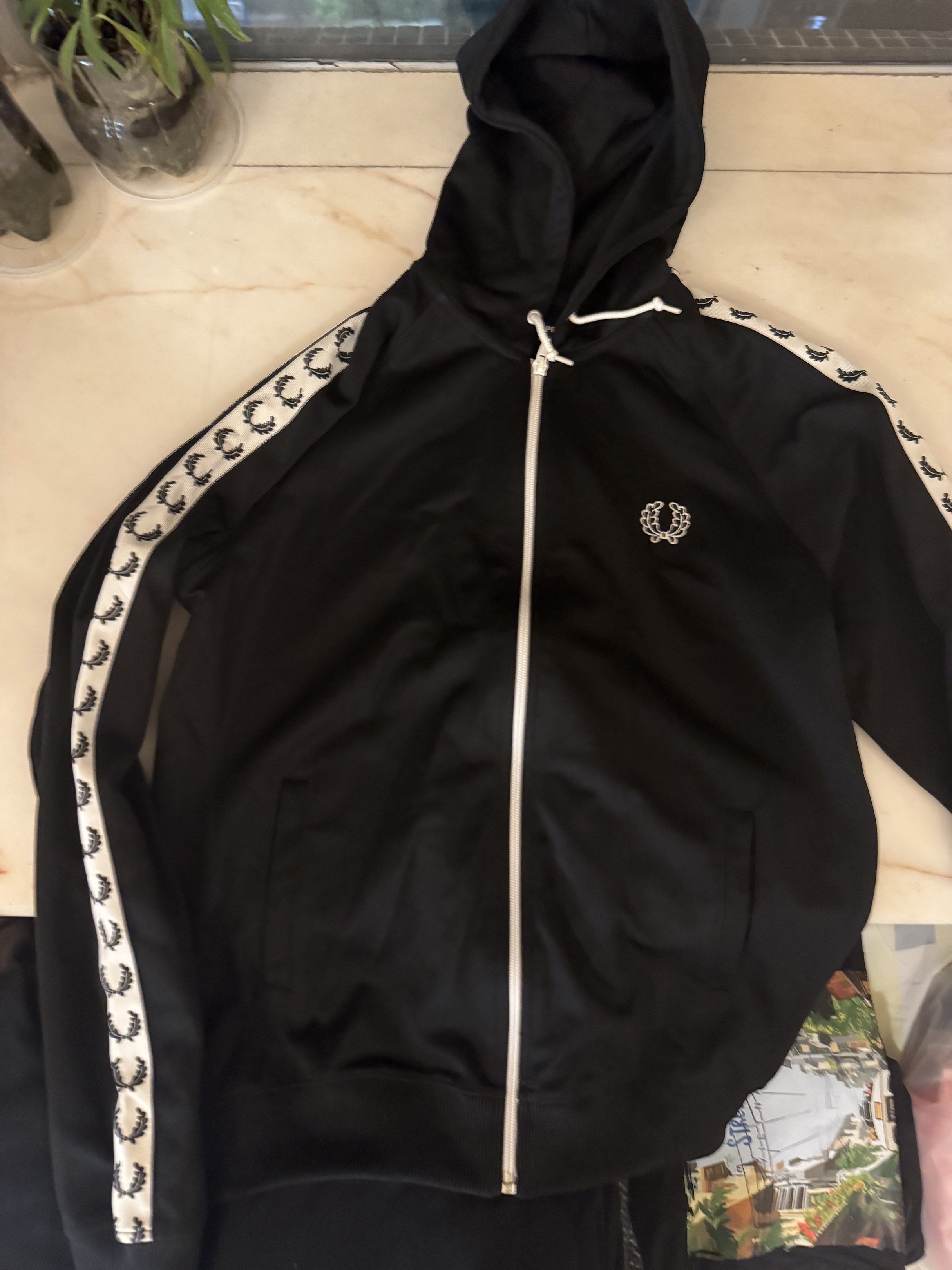Fred Perry Black Track Jacket （分類：外套及戶外衣服）位於 Hong Kong。 由 rikimaru68 提交（商品編號 1417945649，圖片 2）。簡介： Black Fred Perry track jacket with white detailing on the sleeves. Features a full zip closure and a hood. The Fred Perry logo is embroidered on the chest. Made in Portugal.。