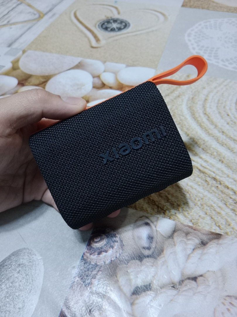 Xiaomi Portable Bluetooth Speaker (Category: Soundbars, Speakers & Amplifiers) located in Marikina City. Submitted by jameeeessssm (Listing ID 1417822153, Image 2). Description: - Xiaomi Mi Sound Pocket 5W portable Bluetooth speaker - Color: Black with orange strap - Features power and Bluetooth buttons - Mesh fabric design - Includes charging port - Xiaomi logo visible - Designed by Xiaomi.