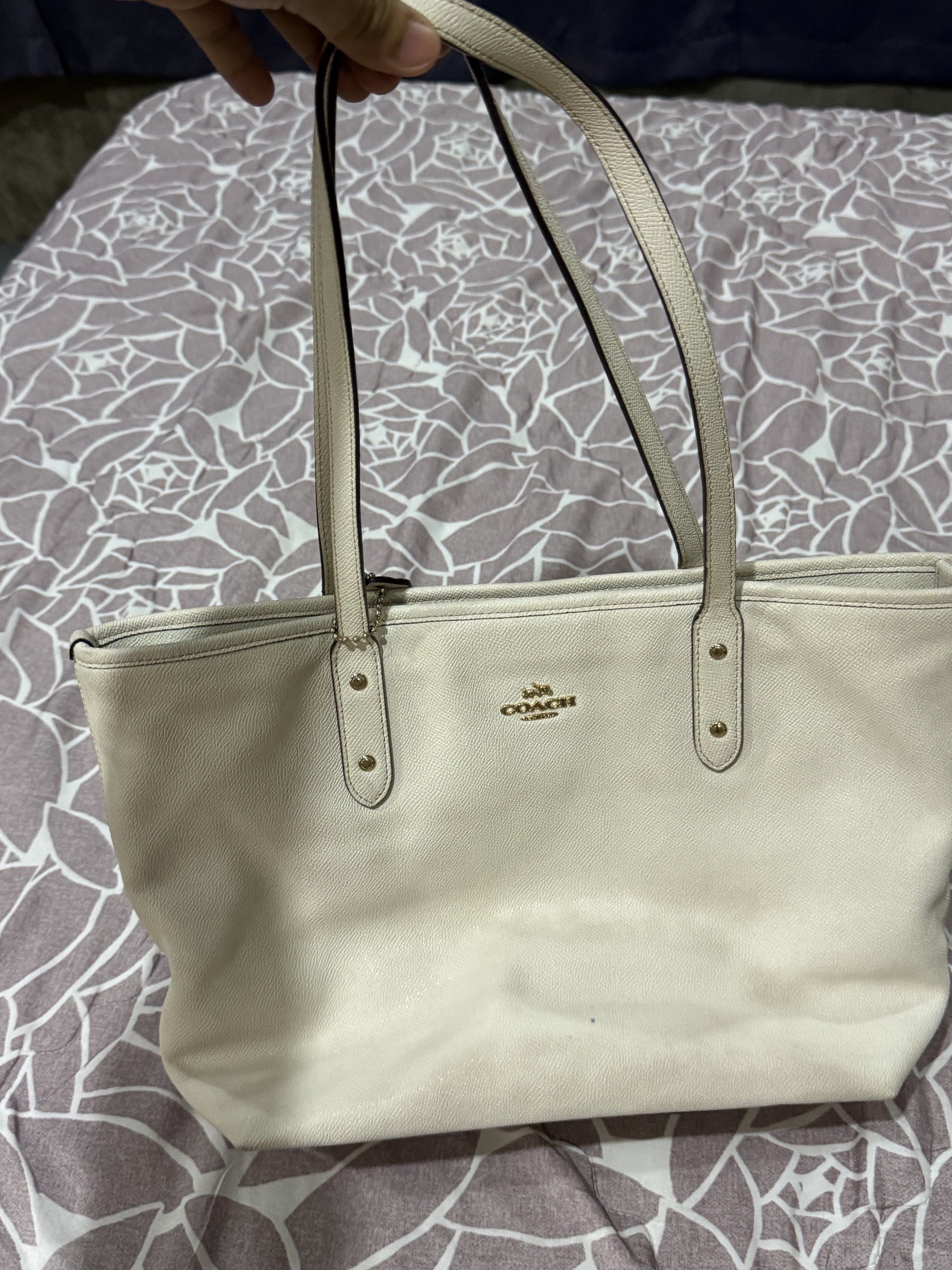 Coach Tote Bag (Category: Luxury Bags & Wallets) located in Sual. Submitted by Twinkle (Listing ID 1418155849, Image 1). Description: - Cream-colored Coach tote bag - Zip closure - Dual top handles - Includes Coach hang tag - Interior: zippered pocket and slip pocket - Gold-tone hardware - Coach logo on front - Dark interior lining - with signs of usages and discoloration that's not obvious.