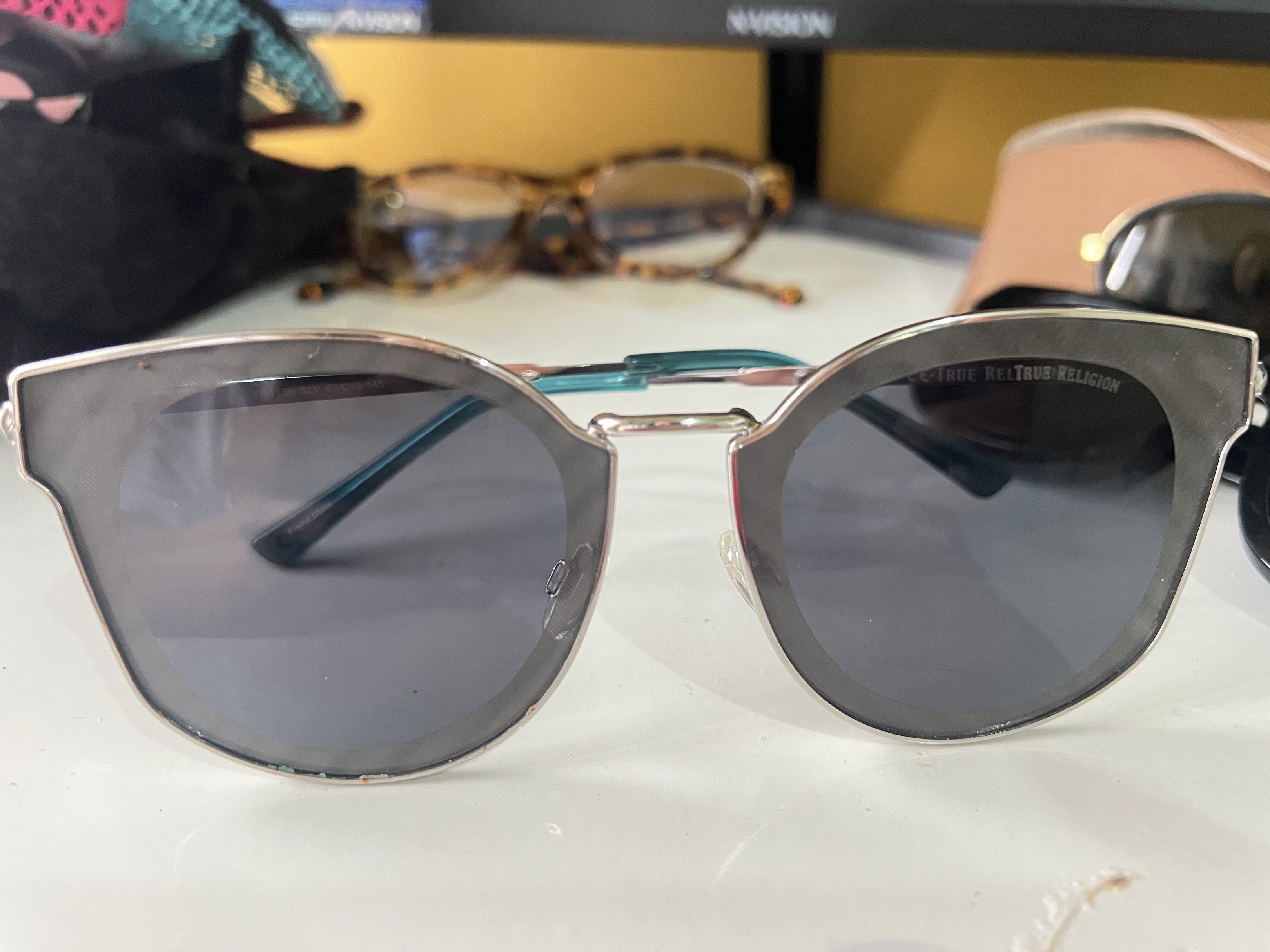 True Religion Sunglasses (Category: Sunglasses & Eyewear) located in Quezon City. Submitted by bubspreloved (Listing ID 1418080683, Image 1). Description: - True Religion sunglasses - Silver frame - Dark lenses - Teal accents on arms - True Religion logo visible - Stylish and fashionable.