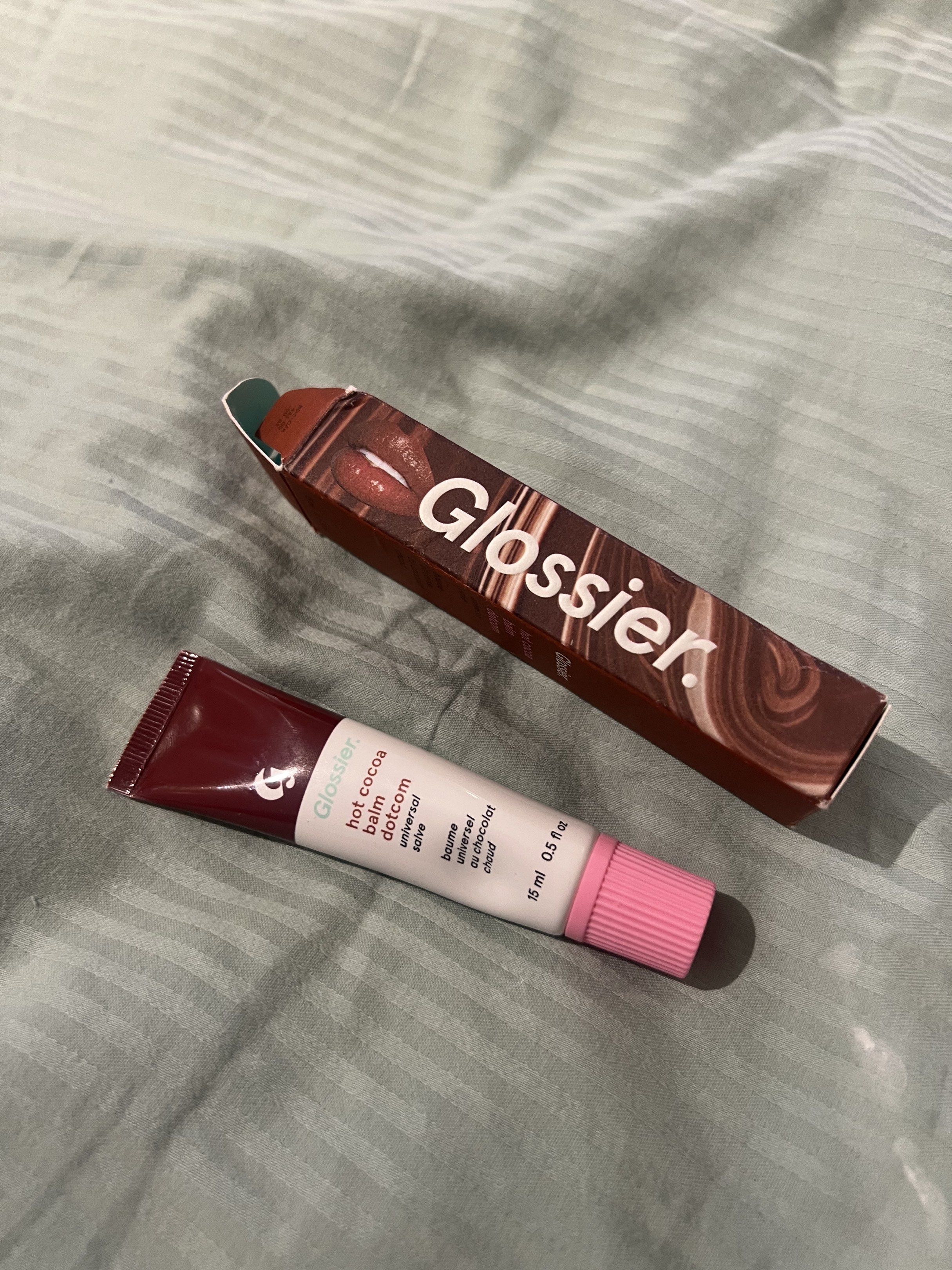 Glossier Hot Cocoa Balm Dotcom (Category: Makeup) located in Taguig. Submitted by new_again_ (Listing ID 1418324867, Image 1). Description: - Glossier Hot Cocoa Balm Dotcom - Scent: Hot Cocoa - Size: 15 ml / 0.5 fl oz - Packaging: Brown box with marshmallow design.