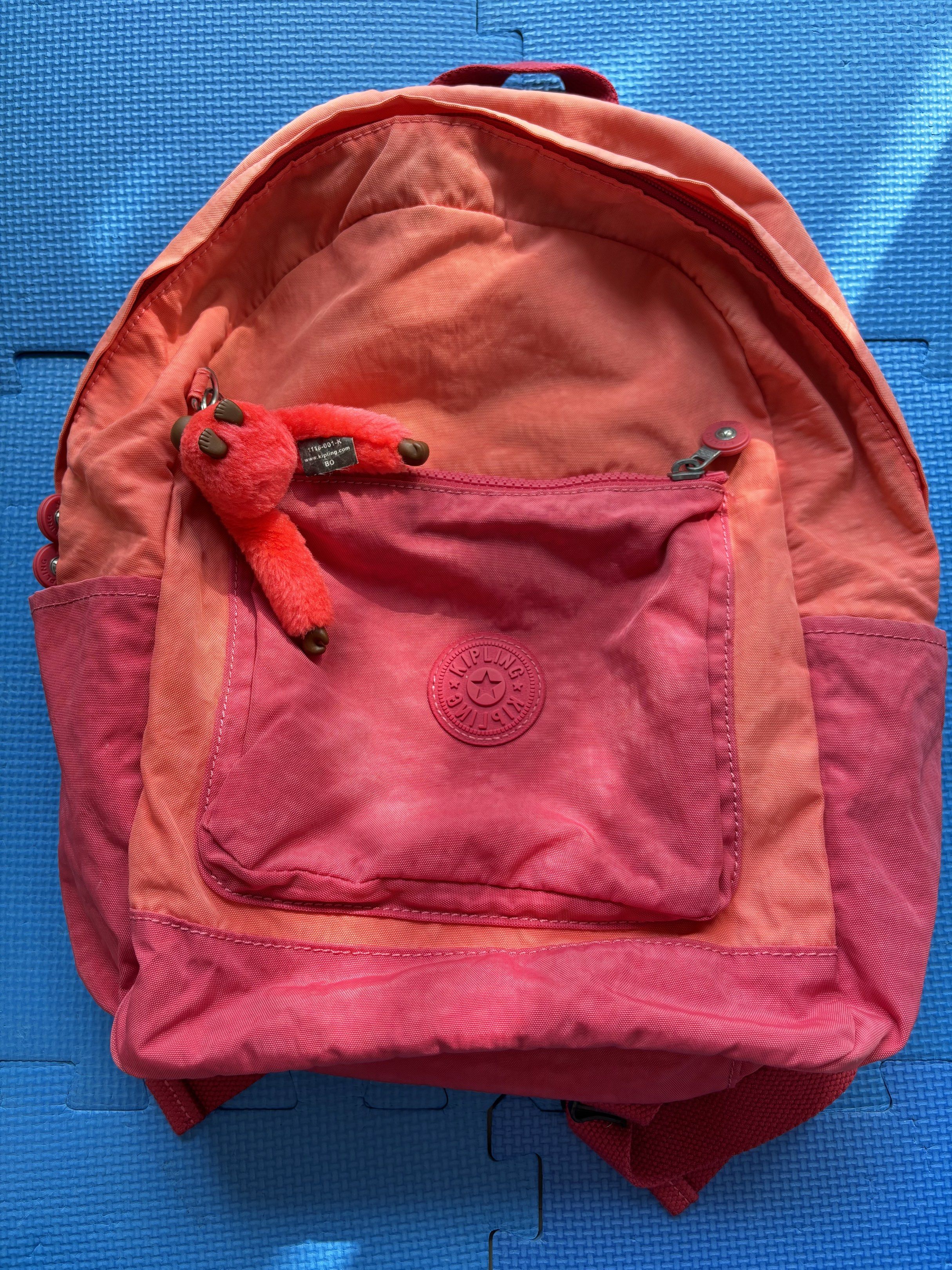 Kipling Backpack （分類：背囊）位於 Hong Kong。 由 carcaca 提交（商品編號 1418322258，圖片 1）。簡介： Kipling backpack features a vibrant pink and orange color scheme. It has a front pocket with the Kipling logo and comes with a small monkey keychain. The backpack has adjustable shoulder straps and a top handle. The back of the backpack has a zipper pocket.。