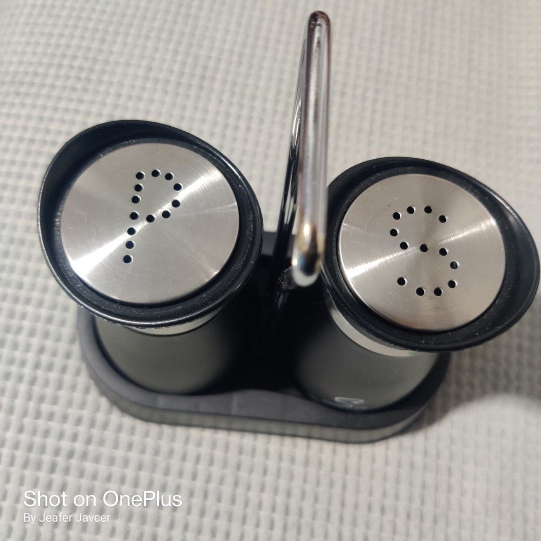 Salt and Pepper Shaker Set with Stand (Category: Other Kitchenware & Tableware) located in Baguio. Submitted by ferns_garage.0924 (Listing ID 1418346948, Image 3). Description: - Set includes salt and pepper shakers. - Sleek black design with stainless steel accents. - Clearly labeled for easy identification. - Comes with a convenient stand for organized storage. - Pepper shaker has arrow-shaped holes. - Salt shaker has circle-shaped holes. scan 