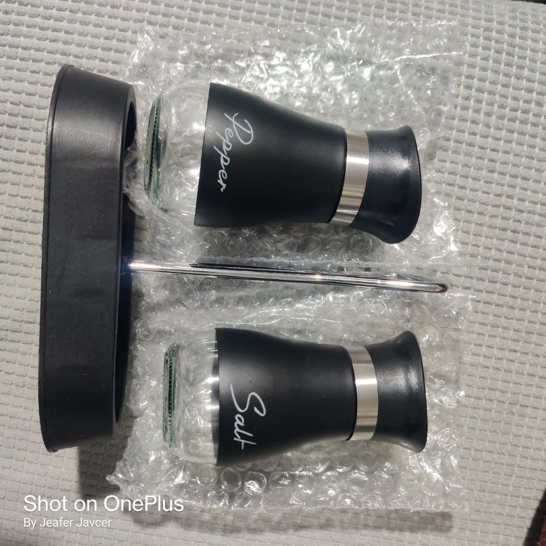 Salt and Pepper Shaker Set with Stand (Category: Other Kitchenware & Tableware) located in Baguio. Submitted by ferns_garage.0924 (Listing ID 1418346948, Image 1). Description: - Set includes salt and pepper shakers. - Sleek black design with stainless steel accents. - Clearly labeled for easy identification. - Comes with a convenient stand for organized storage. - Pepper shaker has arrow-shaped holes. - Salt shaker has circle-shaped holes. scan 