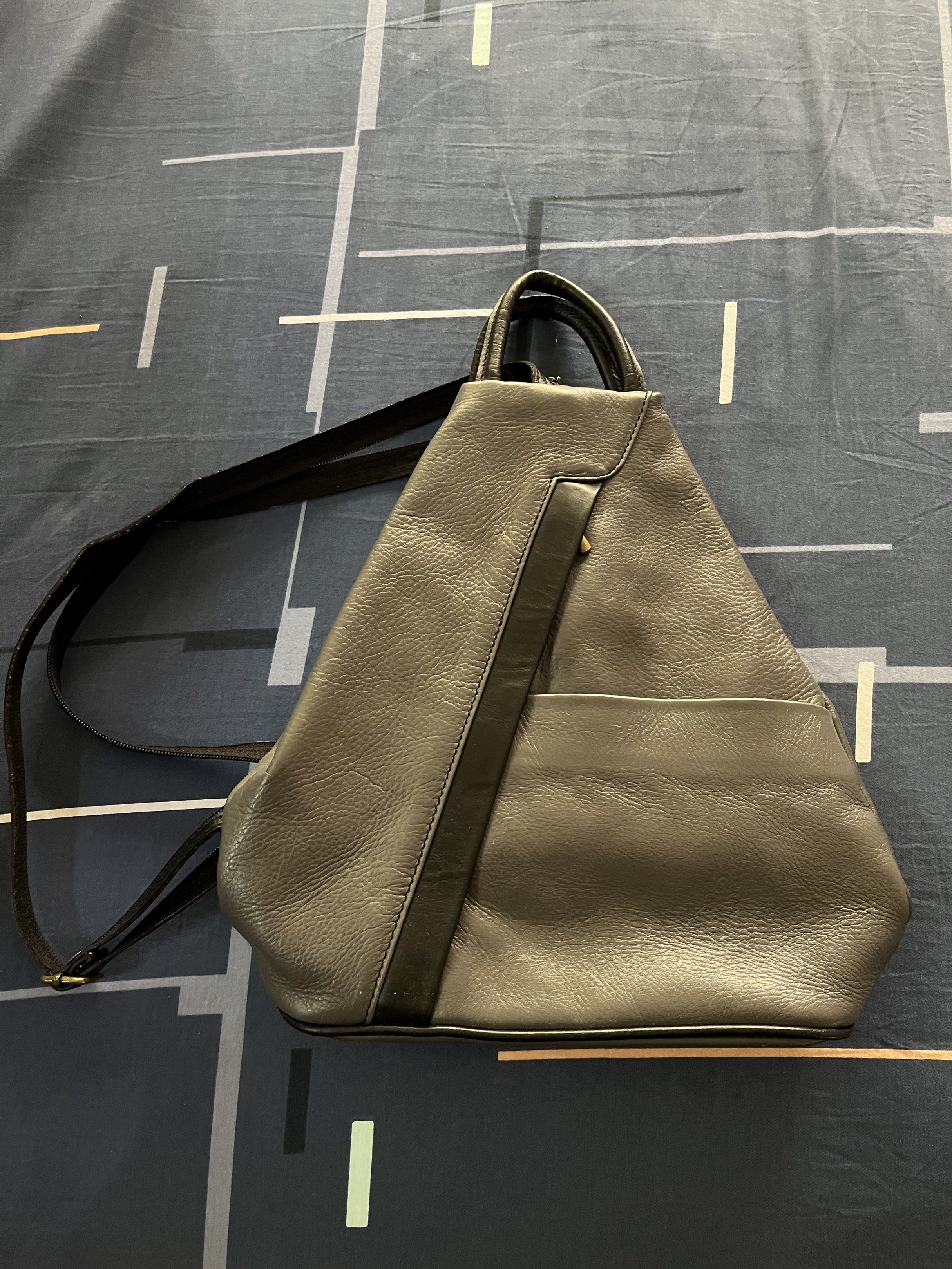 Sling/triangular Grey Leather Backpack (Category: Backpacks) located in Las Pinas. Submitted by sortandsimplify (Listing ID 1418403054, Image 1). Description: - Stylish grey leather backpack - Unique triangular design - Front pocket - Top handle - Adjustable straps - Zipper closure - Perfect for everyday use or travel.