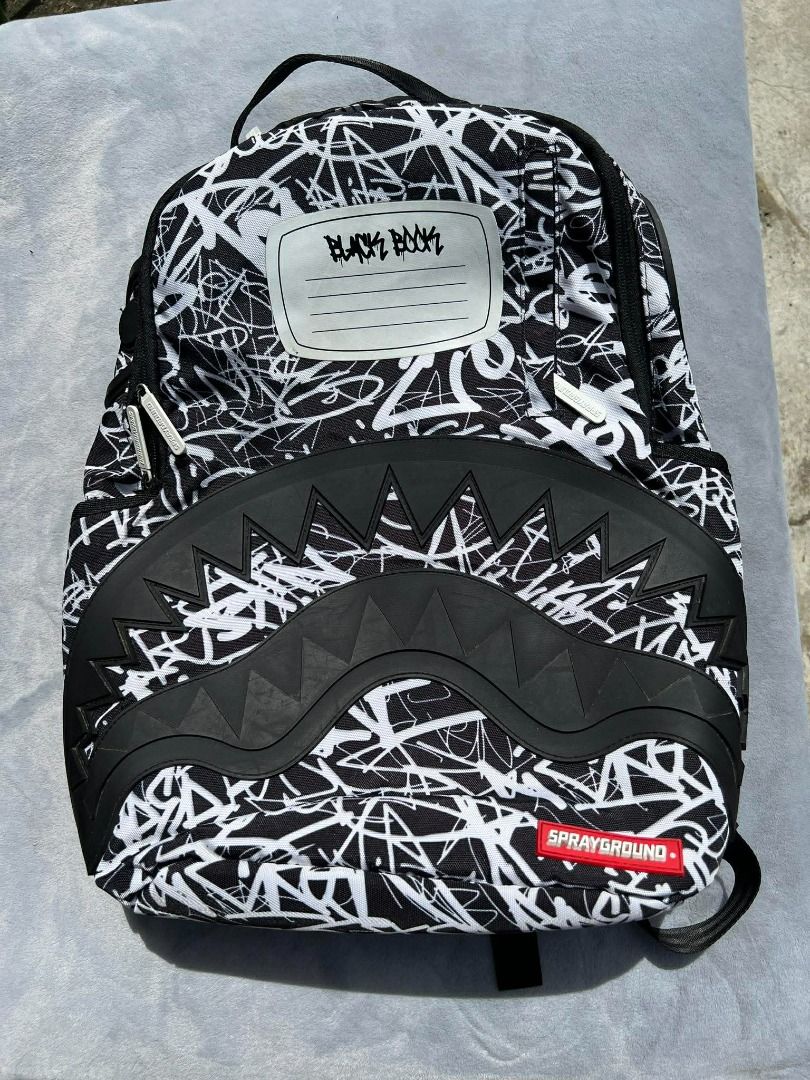 Sprayground Black Book Backpack Brand New (Category: Backpacks) located in Lipa City. Submitted by wewez_store (Listing ID 1418332794, Image 1). Description: - Sprayground backpack with a unique black and white design. - Features a bold shark mouth design on the front. - Includes a "BLACK BOOK" label area. - Equipped with a top handle and adjustable straps for comfort. - Features the Sprayground logo on the bottom right..