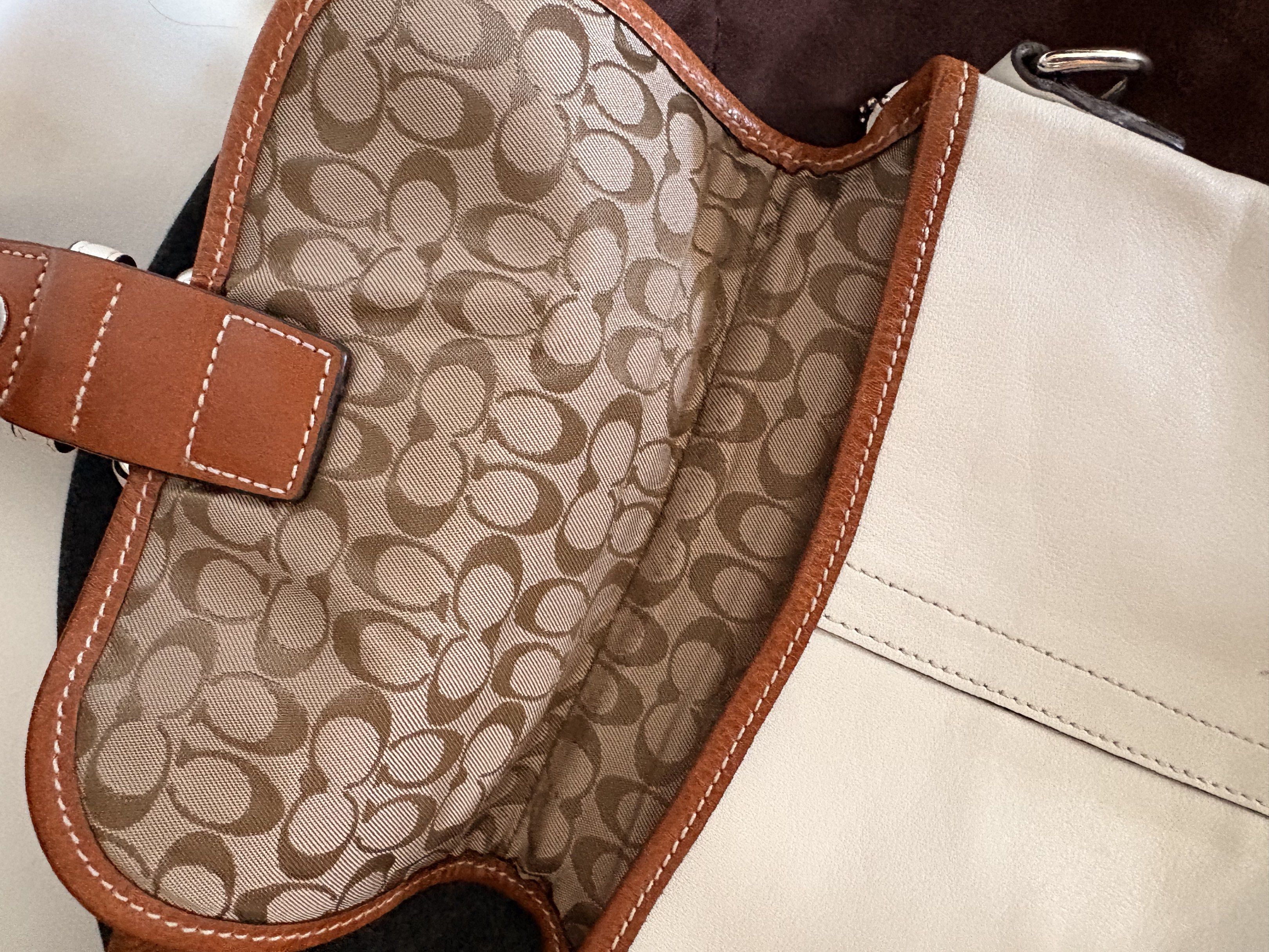AUTHENTIC Coach White Leather Crossbody Bag (Category: Luxury Bags & Wallets) located in Baguio. Submitted by luxxycloset (Listing ID 1418453007, Image 3). Description: - Authentic Coach crossbody bag - White leather exterior with brown trim - Silver buckle closure - Adjustable brown strap - Fabric interior with Coach logo - Includes dust bag and Coach hang tag - Dimensions: Approximately 20cm (width) x 23cm (height).