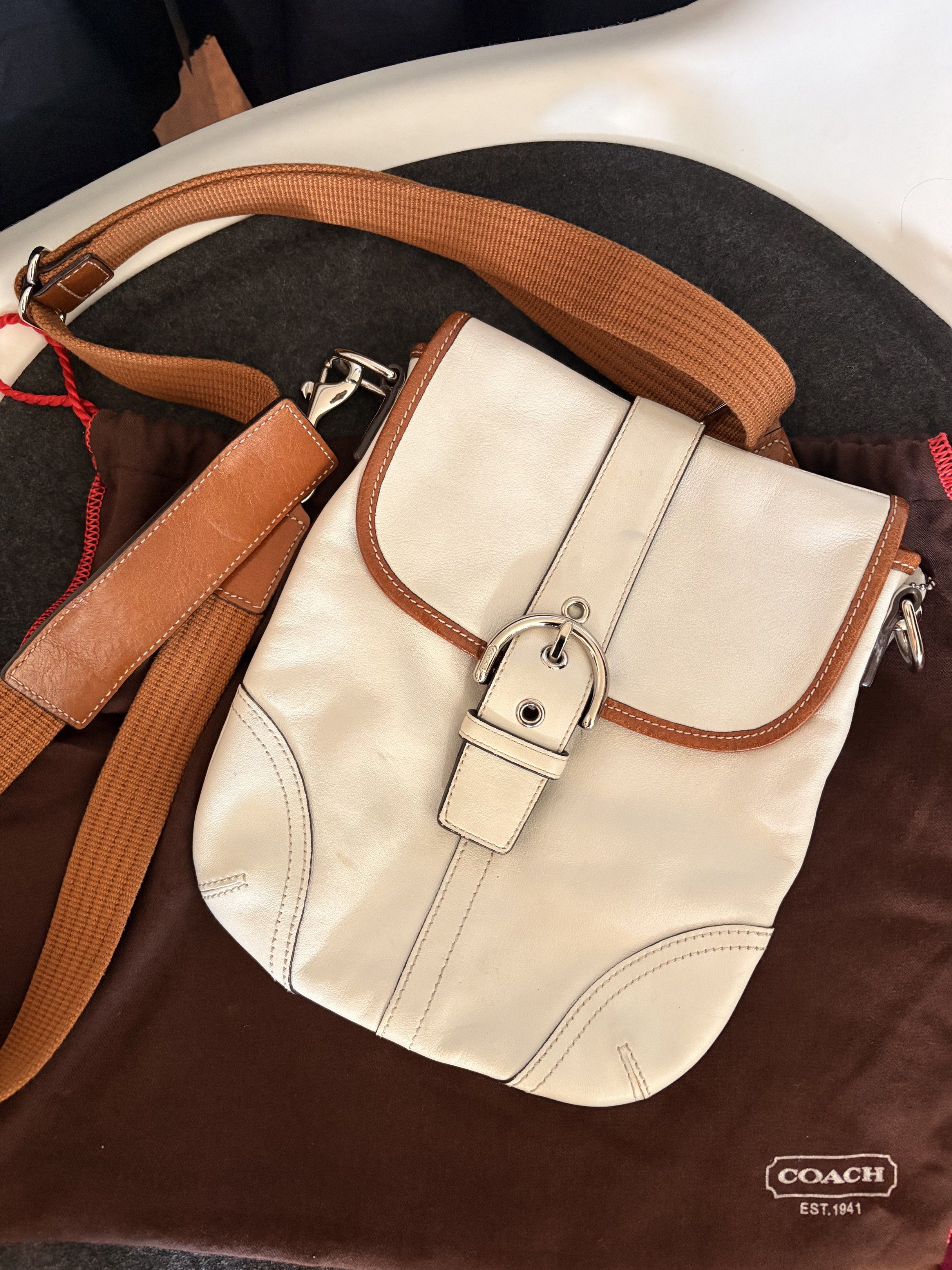 AUTHENTIC Coach White Leather Crossbody Bag (Category: Luxury Bags & Wallets) located in Baguio. Submitted by luxxycloset (Listing ID 1418453007, Image 1). Description: - Authentic Coach crossbody bag - White leather exterior with brown trim - Silver buckle closure - Adjustable brown strap - Fabric interior with Coach logo - Includes dust bag and Coach hang tag - Dimensions: Approximately 20cm (width) x 23cm (height).