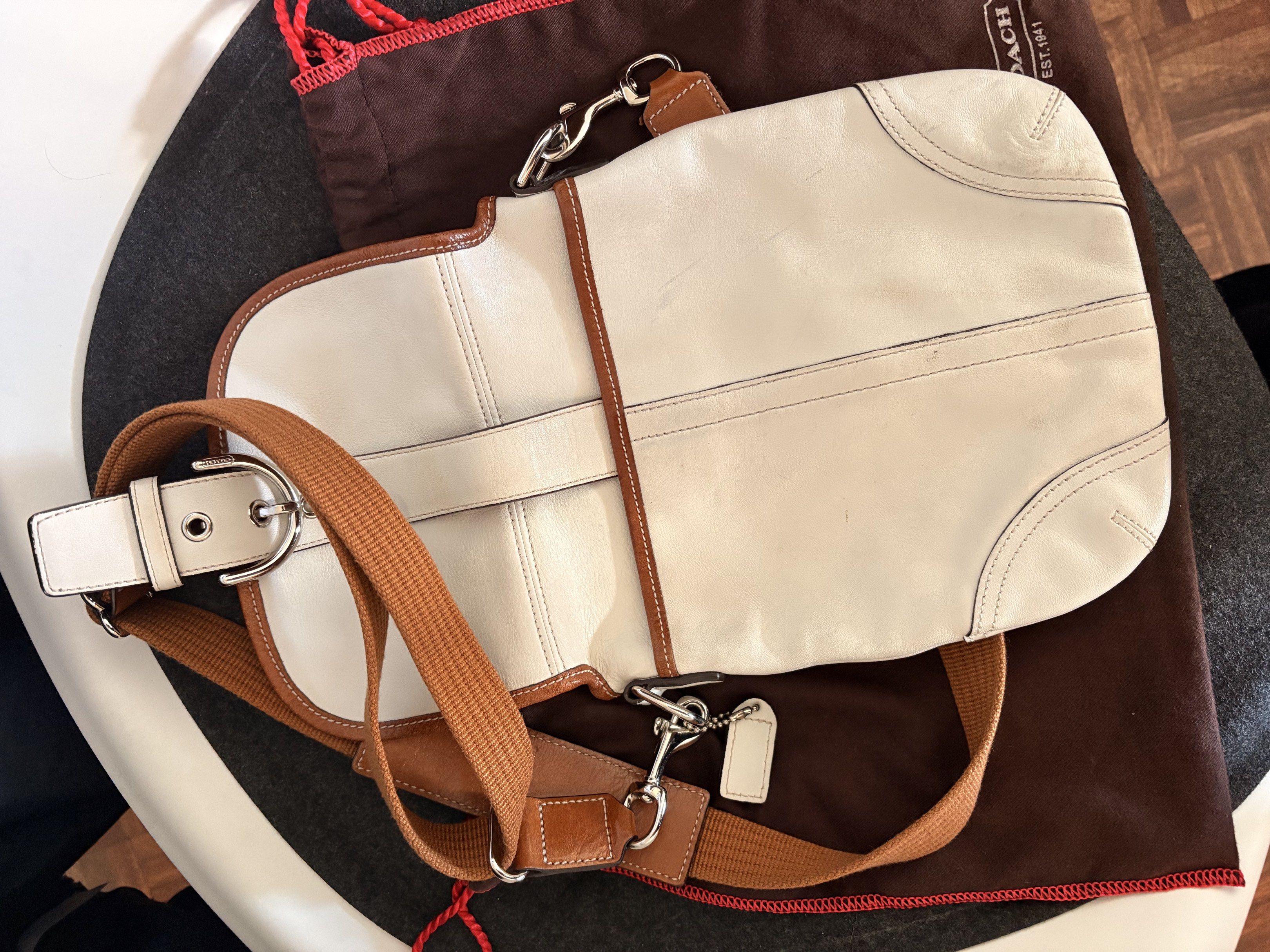AUTHENTIC Coach White Leather Crossbody Bag (Category: Luxury Bags & Wallets) located in Baguio. Submitted by luxxycloset (Listing ID 1418453007, Image 2). Description: - Authentic Coach crossbody bag - White leather exterior with brown trim - Silver buckle closure - Adjustable brown strap - Fabric interior with Coach logo - Includes dust bag and Coach hang tag - Dimensions: Approximately 20cm (width) x 23cm (height).