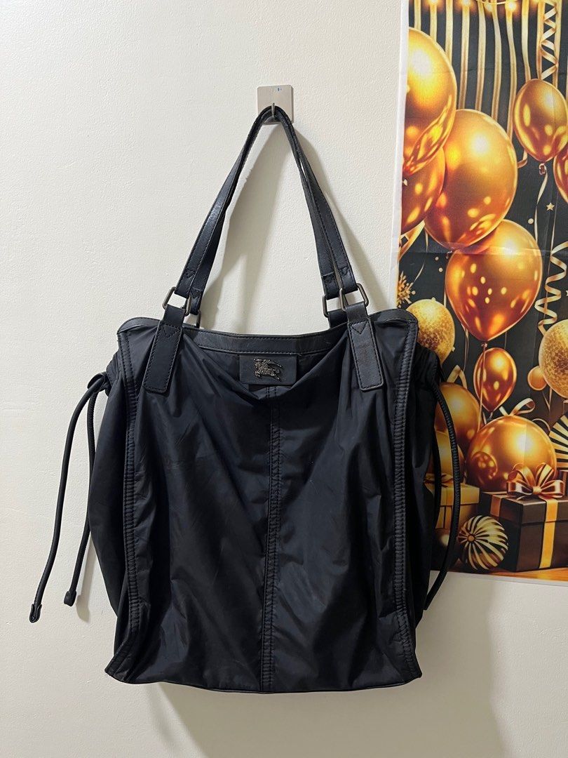 Burberry Black Tote Bag (Category: Luxury Bags & Wallets) located in Caloocan City. Submitted by pumarenluc79160 (Listing ID 1418555363, Image 1). Description: - Authentic Burberry tote bag - Classic black design - Drawstring closure on sides - Signature Burberry check interior lining - Includes an internal zipper pocket - Durable leather handles and trim - Burberry logo detailing on front and inside.