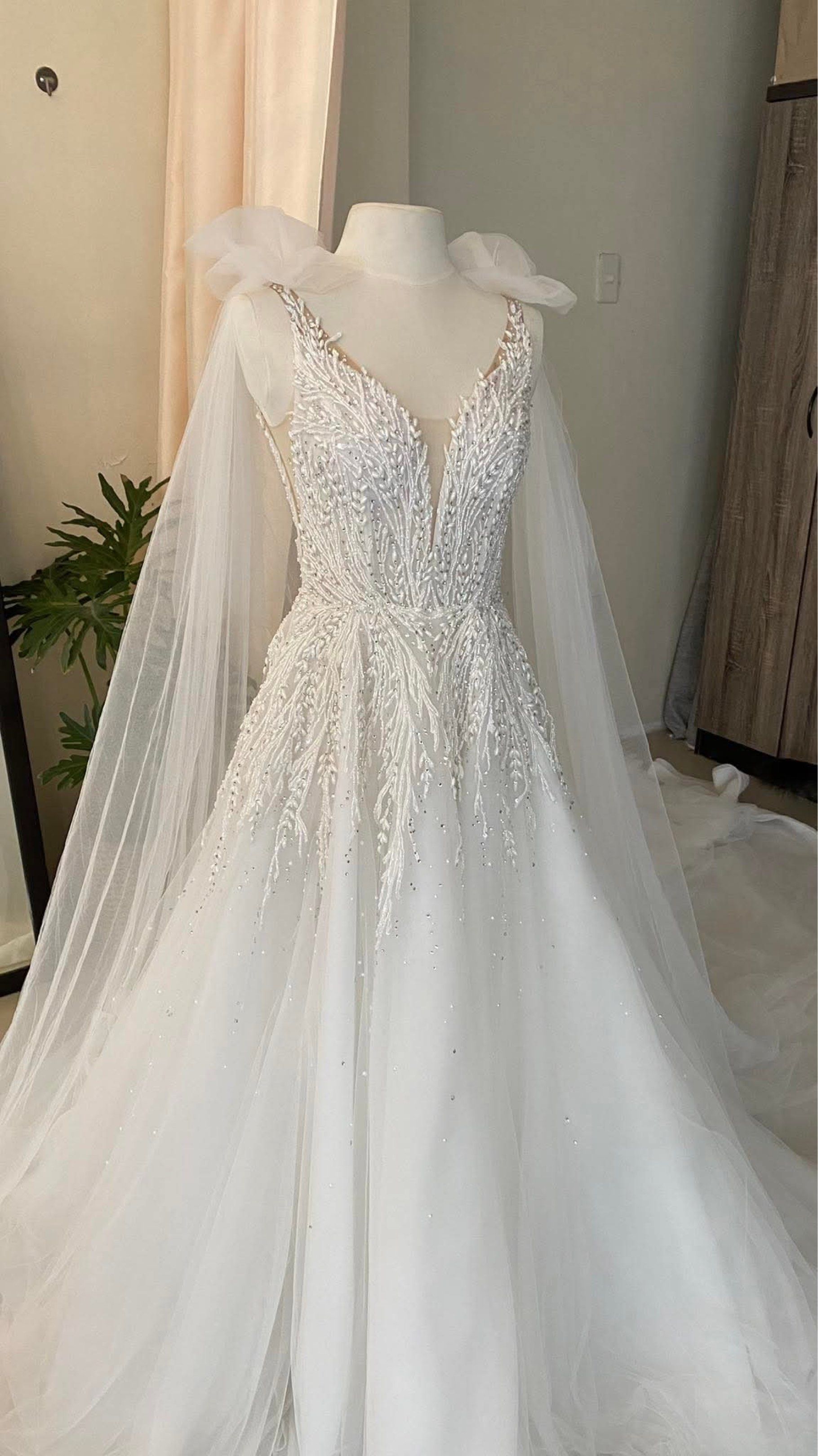 Elegant White Wedding Gown with Cape (Category: Evening dresses & gowns) located in Lipa City. Submitted by lvthrift (Listing ID 1418538183, Image 1). Description: - White wedding gown - Intricate beadwork on bodice - Flowing tulle skirt - Delicate cape detail - Deep V-neckline - Low back - Perfect for a romantic and sophisticated bride.