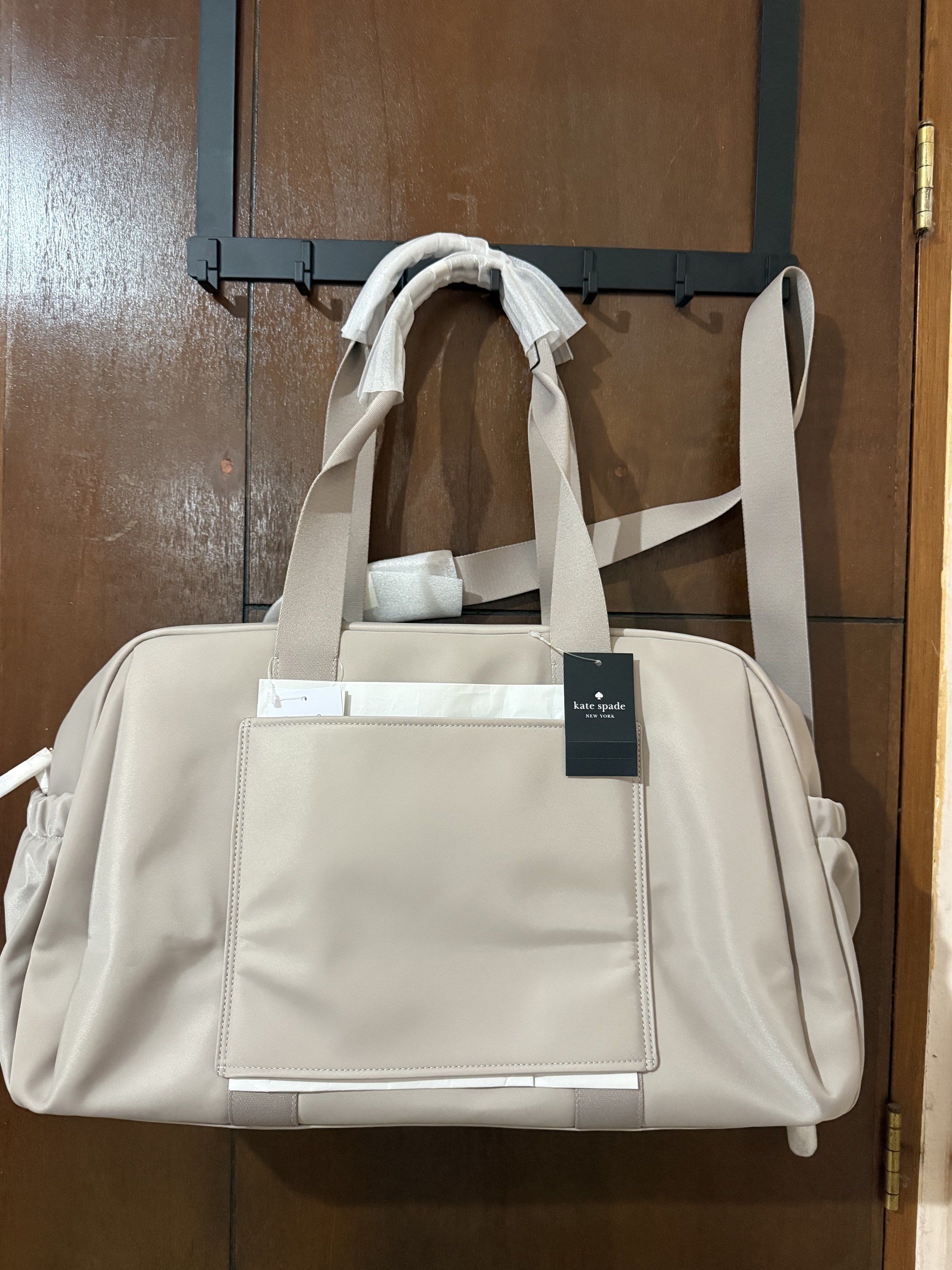 Kate Spade Weekender Bag (Category: Luxury Bags & Wallets) located in Paranaque City. Submitted by aaaaa_earth (Listing ID 1418541606, Image 2). Description: Kate Spade Weekender bag is a stylish and spacious carryall. It features a neutral color, a shoulder strap, and tote handles. The bag has the Kate Spade logo on the front and on the strap. The bag has a large main compartment and an exterior pocket. Color: Cozy Grey .