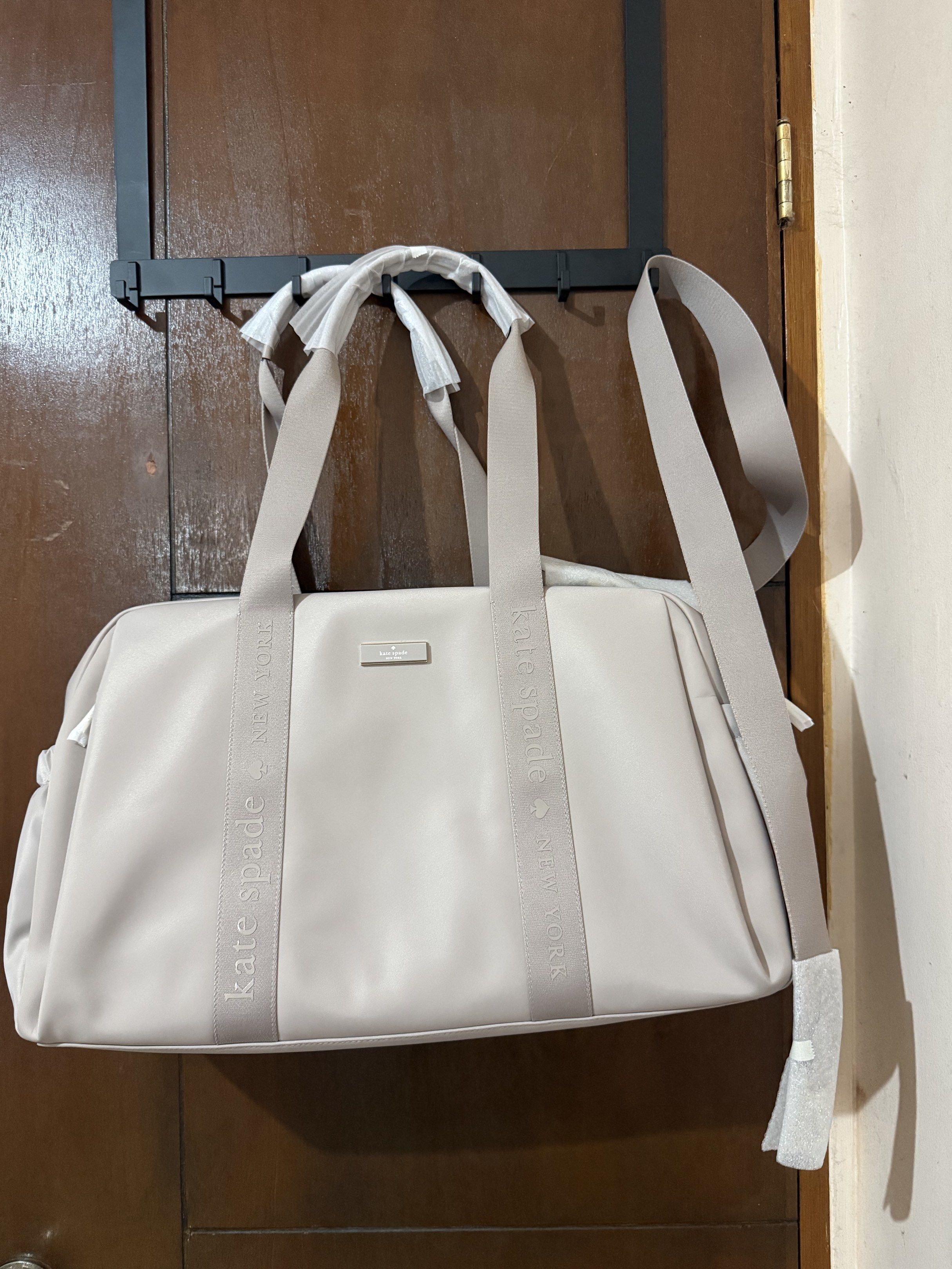 Kate Spade Weekender Bag (Category: Luxury Bags & Wallets) located in Paranaque City. Submitted by aaaaa_earth (Listing ID 1418541606, Image 1). Description: Kate Spade Weekender bag is a stylish and spacious carryall. It features a neutral color, a shoulder strap, and tote handles. The bag has the Kate Spade logo on the front and on the strap. The bag has a large main compartment and an exterior pocket. Color: Cozy Grey .