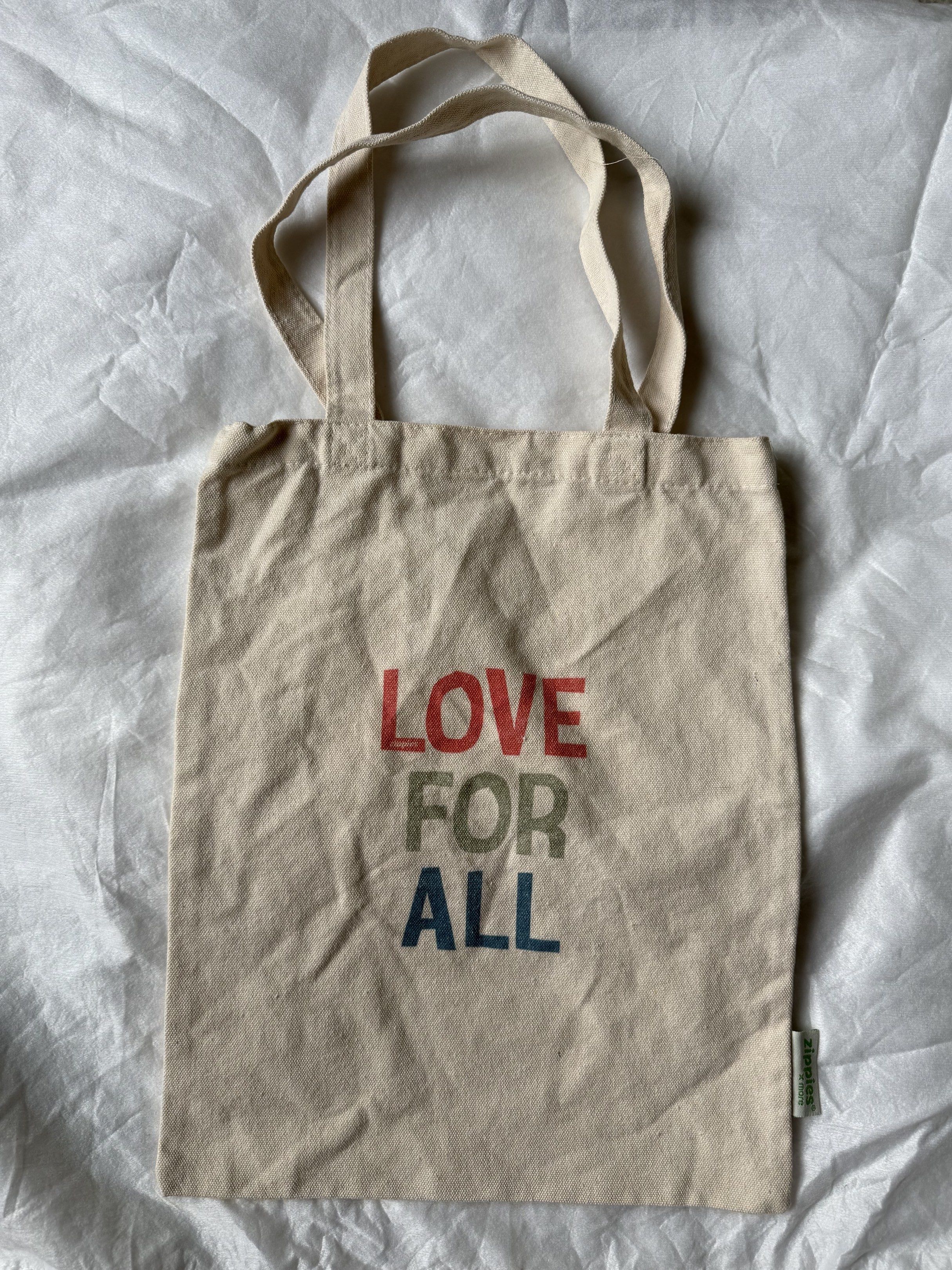 Love For All Tote Bag (Category: Tote Bags) located in Manila. Submitted by stuffcartph (Listing ID 1418426842, Image 1). Description: - Beige tote bag - Features "LOVE FOR ALL" print - Two handles for carrying - Includes a small side tag - Plain back - Ideal for everyday use.