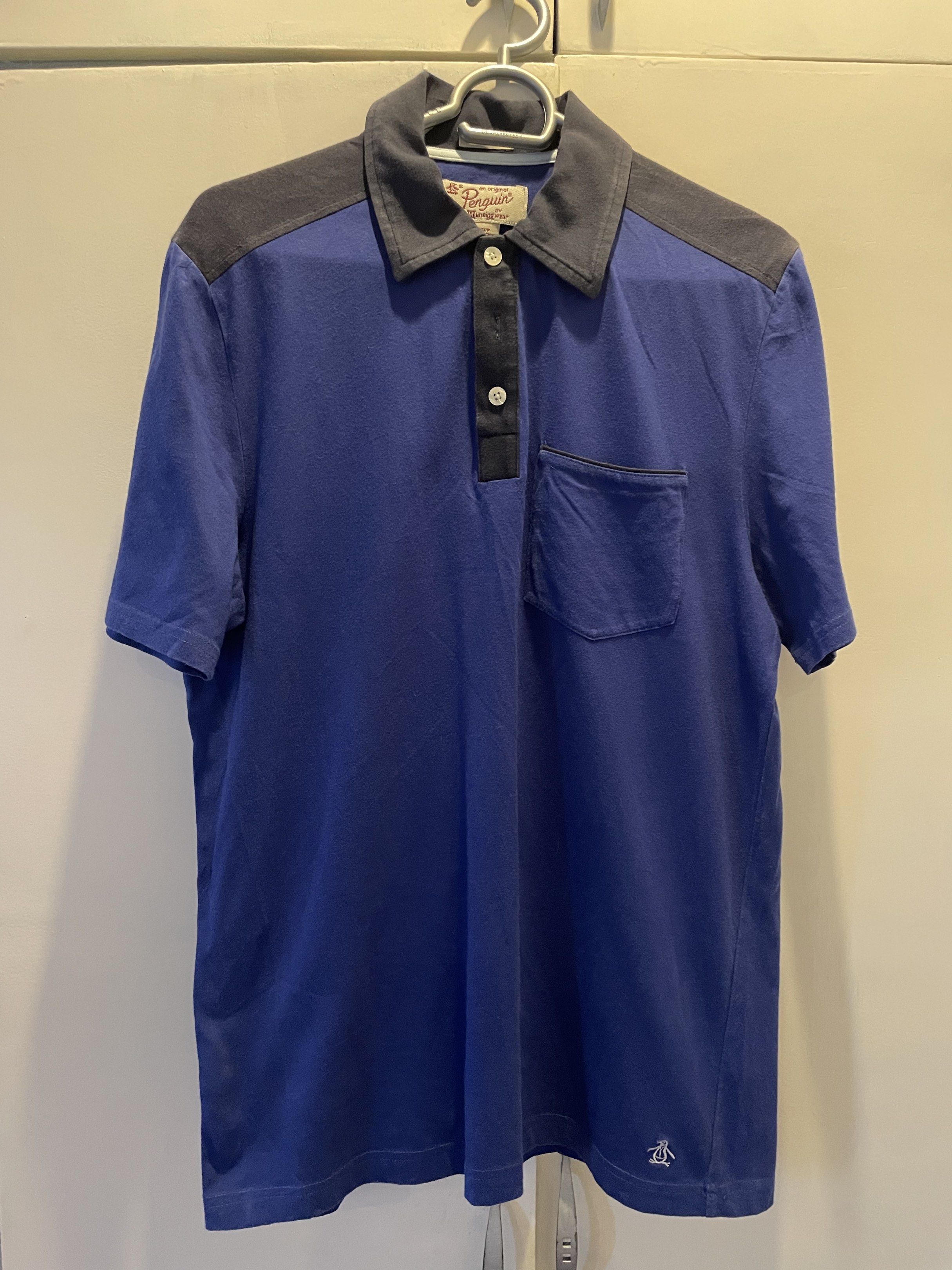 Original Penguin Polo Shirt (Category: Tshirts & Polo Shirts ) located in Las Pinas. Submitted by bmtl_ (Listing ID 1418526051, Image 1). Description: Original Penguin polo shirt in blue with a contrasting grey collar and shoulder panels. Features a pocket on the chest and the iconic Penguin logo embroidered on the bottom. The shirt has a button-up placket and a classic polo collar. Made by Munsingwear..