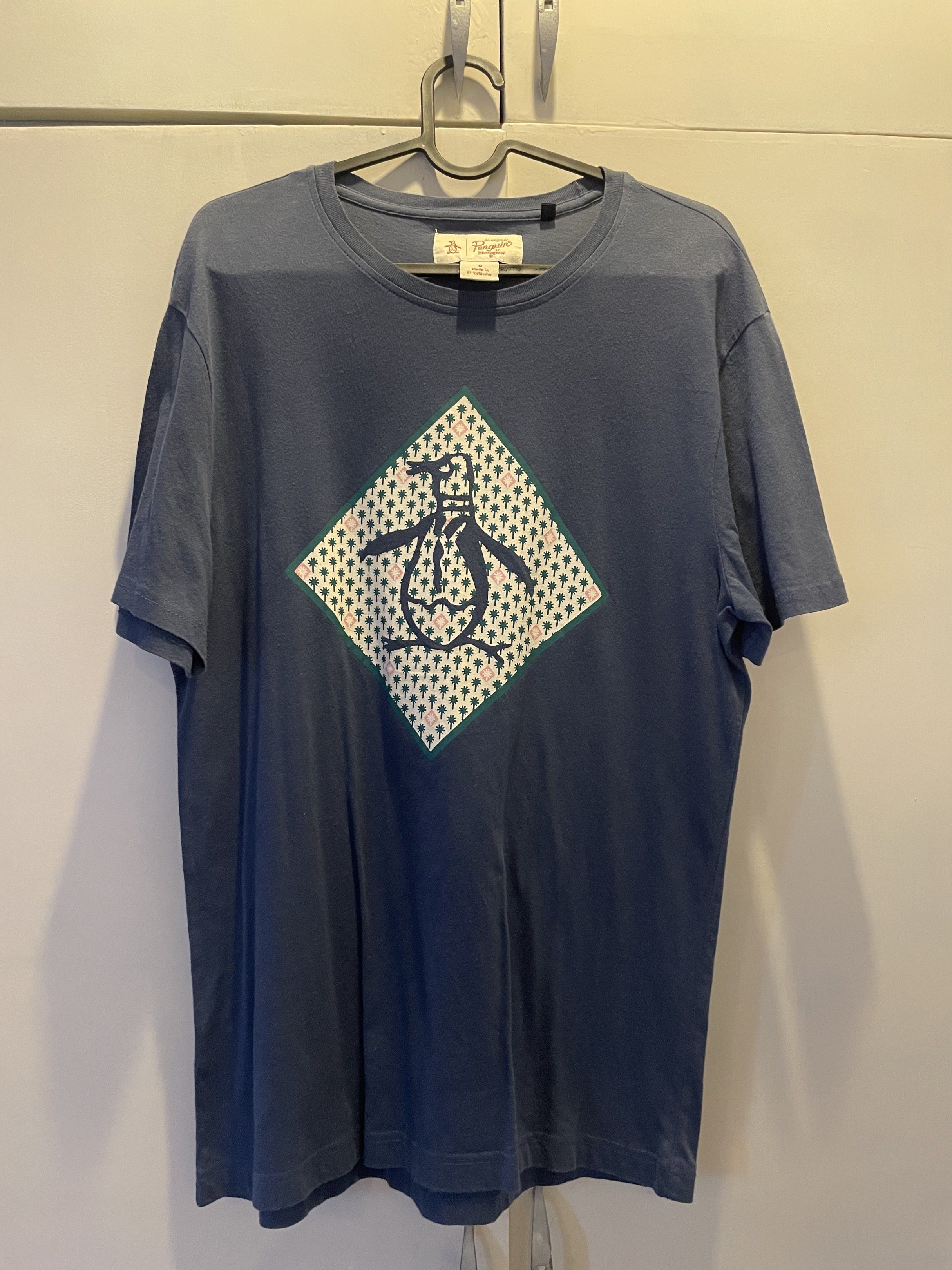 Original Penguin T-shirt - M (Category: Tshirts & Polo Shirts ) located in Las Pinas. Submitted by bmtl_ (Listing ID 1418526197, Image 1). Description: Original Penguin T-shirt in navy blue. Features a diamond-shaped graphic with a penguin logo on the front. The shirt is size M and made in El Salvador. The tag is visible, showing the brand and size. The shirt has short sleeves and a crew neck..