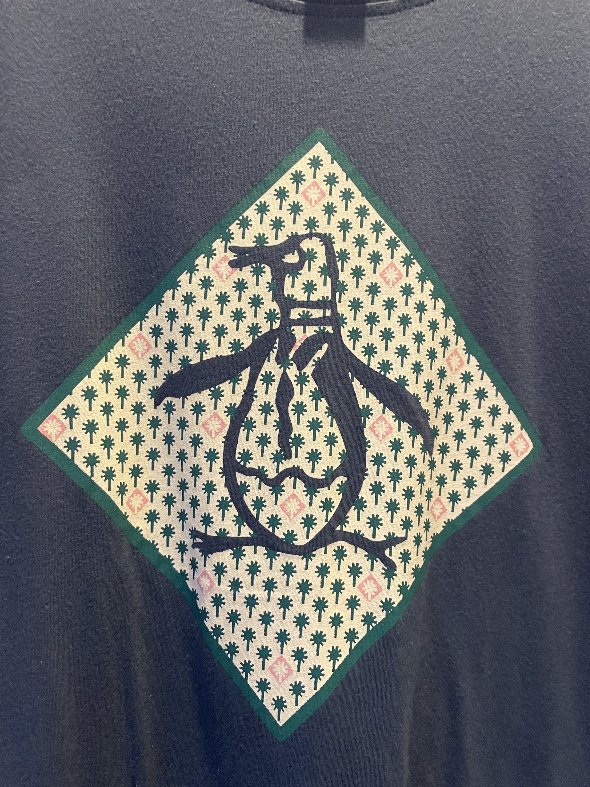 Original Penguin T-shirt - M (Category: Tshirts & Polo Shirts ) located in Las Pinas. Submitted by bmtl_ (Listing ID 1418526197, Image 2). Description: Original Penguin T-shirt in navy blue. Features a diamond-shaped graphic with a penguin logo on the front. The shirt is size M and made in El Salvador. The tag is visible, showing the brand and size. The shirt has short sleeves and a crew neck..