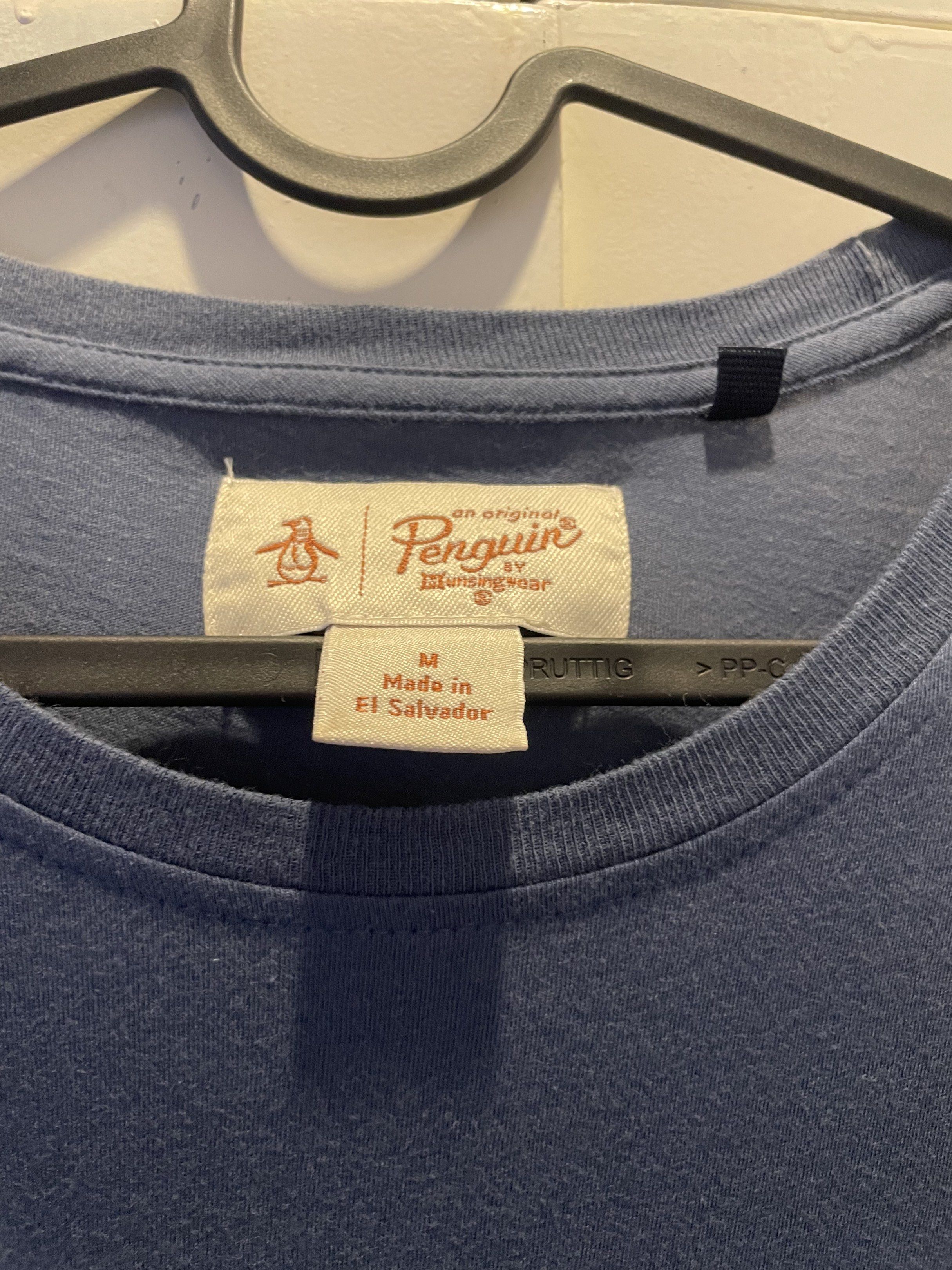 Original Penguin T-shirt - M (Category: Tshirts & Polo Shirts ) located in Las Pinas. Submitted by bmtl_ (Listing ID 1418526197, Image 3). Description: Original Penguin T-shirt in navy blue. Features a diamond-shaped graphic with a penguin logo on the front. The shirt is size M and made in El Salvador. The tag is visible, showing the brand and size. The shirt has short sleeves and a crew neck..