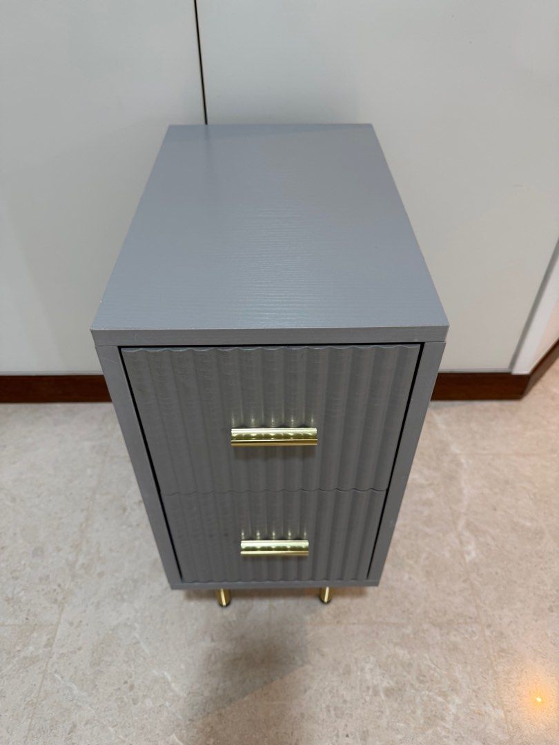 Bedside Table (Category: Tables & Sets) located in Singapore. Submitted by infinity80 (Listing ID 1413241405, Image 3). Description: - Bedside Table with two drawers - Dimensions: 25cm x 40 cm x 55cm (L x W x H) - Textured front design - Sophisticated grey finish - Gold-colored handles and legs - Perfect for bedrooms or living areas.