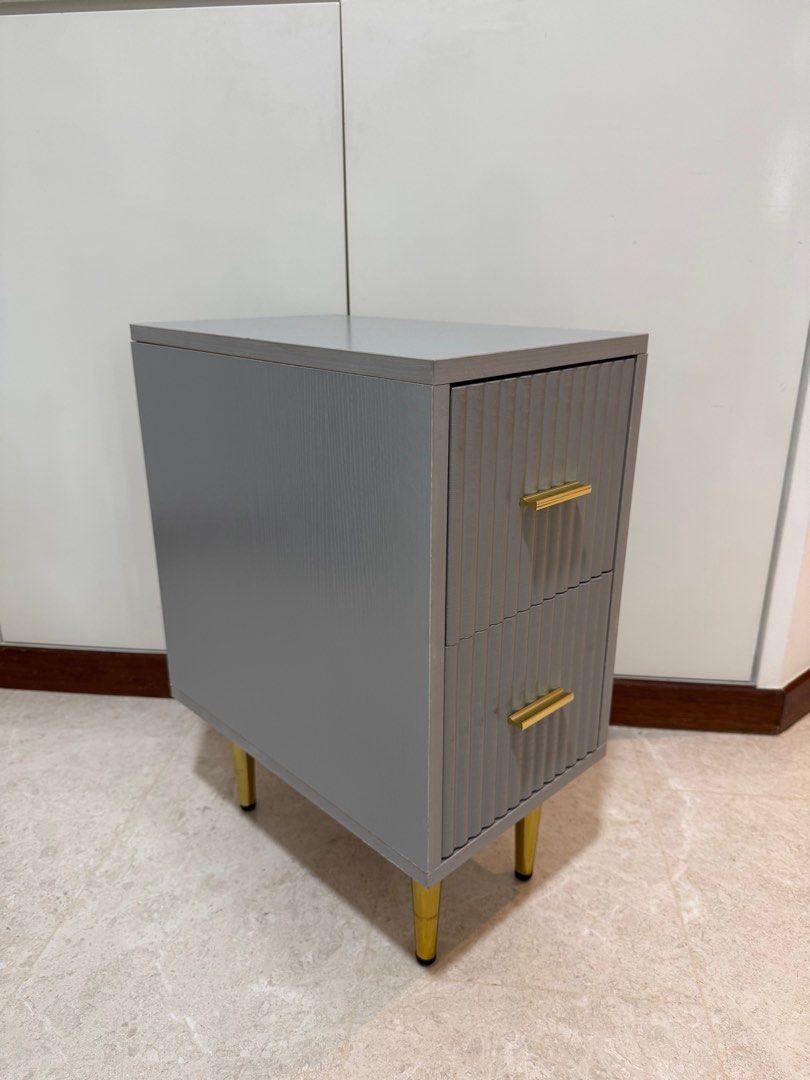 Bedside Table (Category: Tables & Sets) located in Singapore. Submitted by infinity80 (Listing ID 1413241405, Image 2). Description: - Bedside Table with two drawers - Dimensions: 25cm x 40 cm x 55cm (L x W x H) - Textured front design - Sophisticated grey finish - Gold-colored handles and legs - Perfect for bedrooms or living areas.
