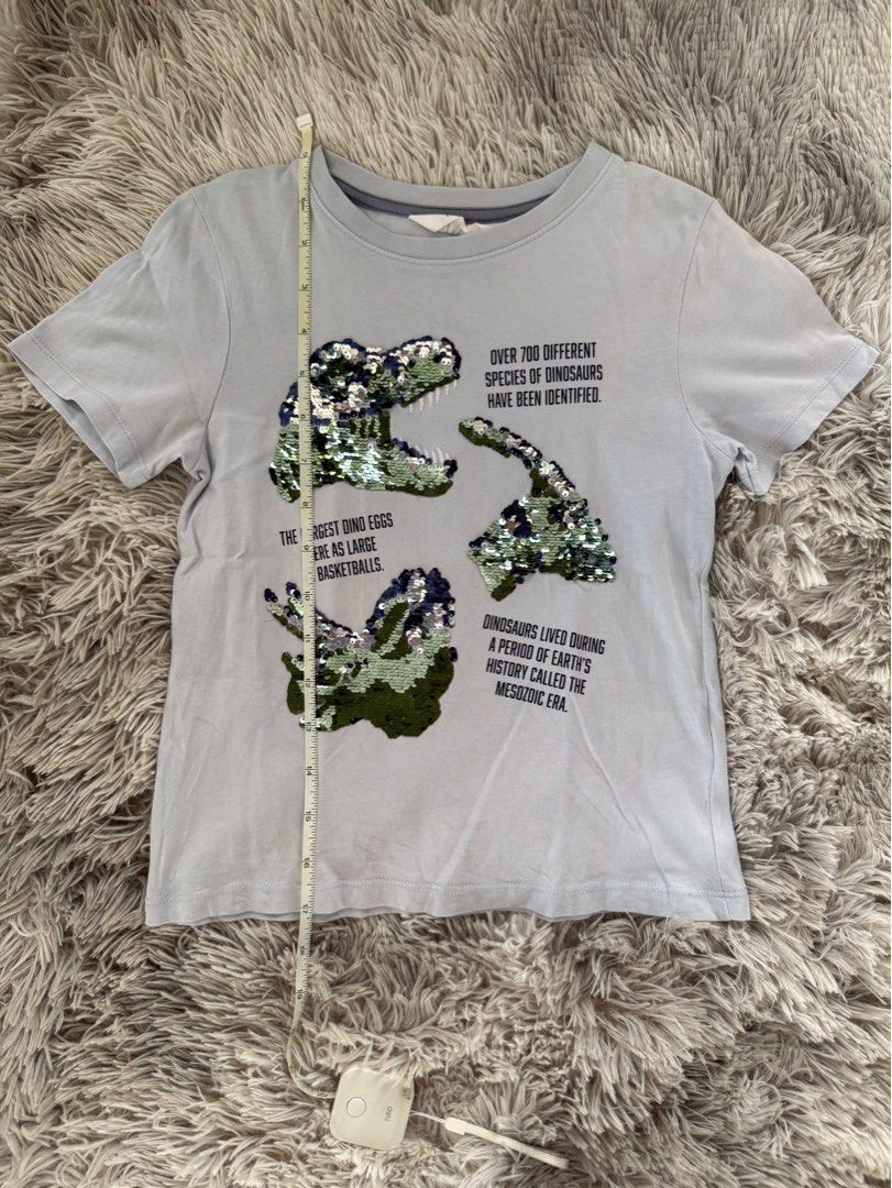 H&M Dinosaur Sequin T-shirt (Category: Babies & Kids Fashion) located in Muntinlupa City. Submitted by caistuff (Listing ID 1413382519, Image 2). Description: LAST PRICE POSTED ALREADY. - H&M t-shirt features a cool dinosaur design with reversible sequins. - Grayish light blue color and short sleeves. - Shirt has text about dinosaurs. - The size is EUR 110/116, US 5T/6, and it is for ages 5-6. - The shirt is made of cotton..