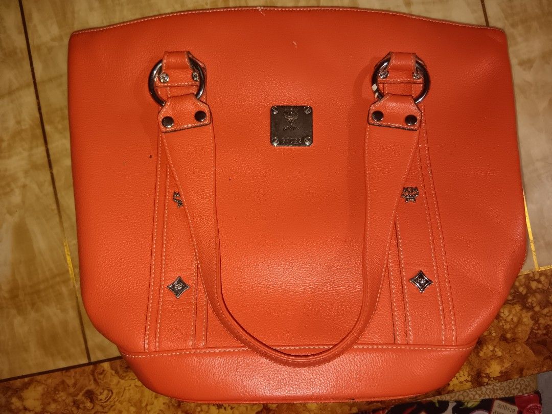MCM Orange Tote Bag (Category: Luxury Bags & Wallets) located in Manila. Submitted by yumirayu (Listing ID 1413225780, Image 1). Description: - Color: Orange - Features double handles with silver hardware - Interior lined with MCM logo fabric - Includes a zippered pocket and additional compartments - Magnetic closure - Exterior shows some wear.