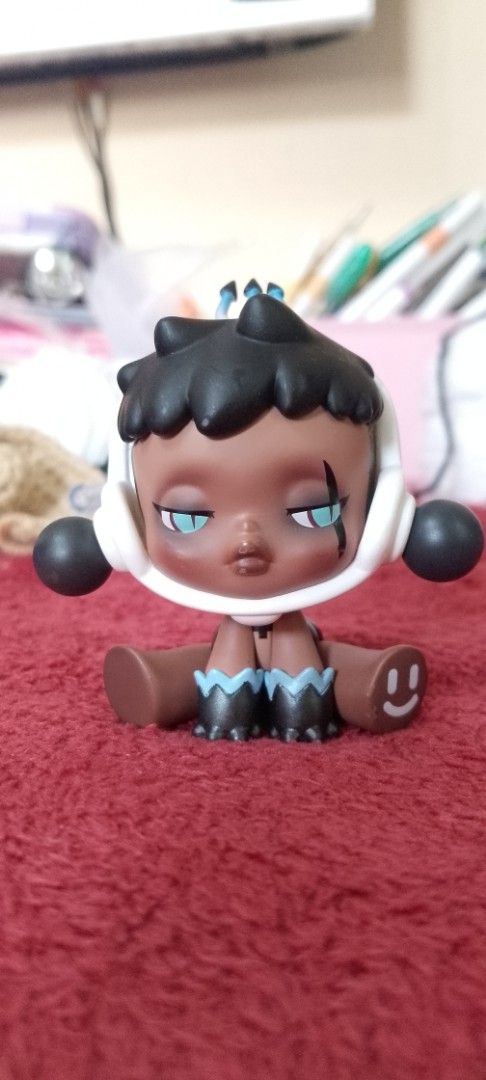 Pop Mart Skullpanda The Warmth Series Figure (Category: Designer & Blind Box Toys) located in Manila. Submitted by titojay (Listing ID 1418659069, Image 1). Description: Collectible figure features a unique design from the Pop Mart Skullpanda The Warmth Series. It has a distinctive appearance with a dark complexion, black hair, and a white headpiece. The figure is in a sitting position with a smiling face on one foot. The Pop Mart and Skullpanda 