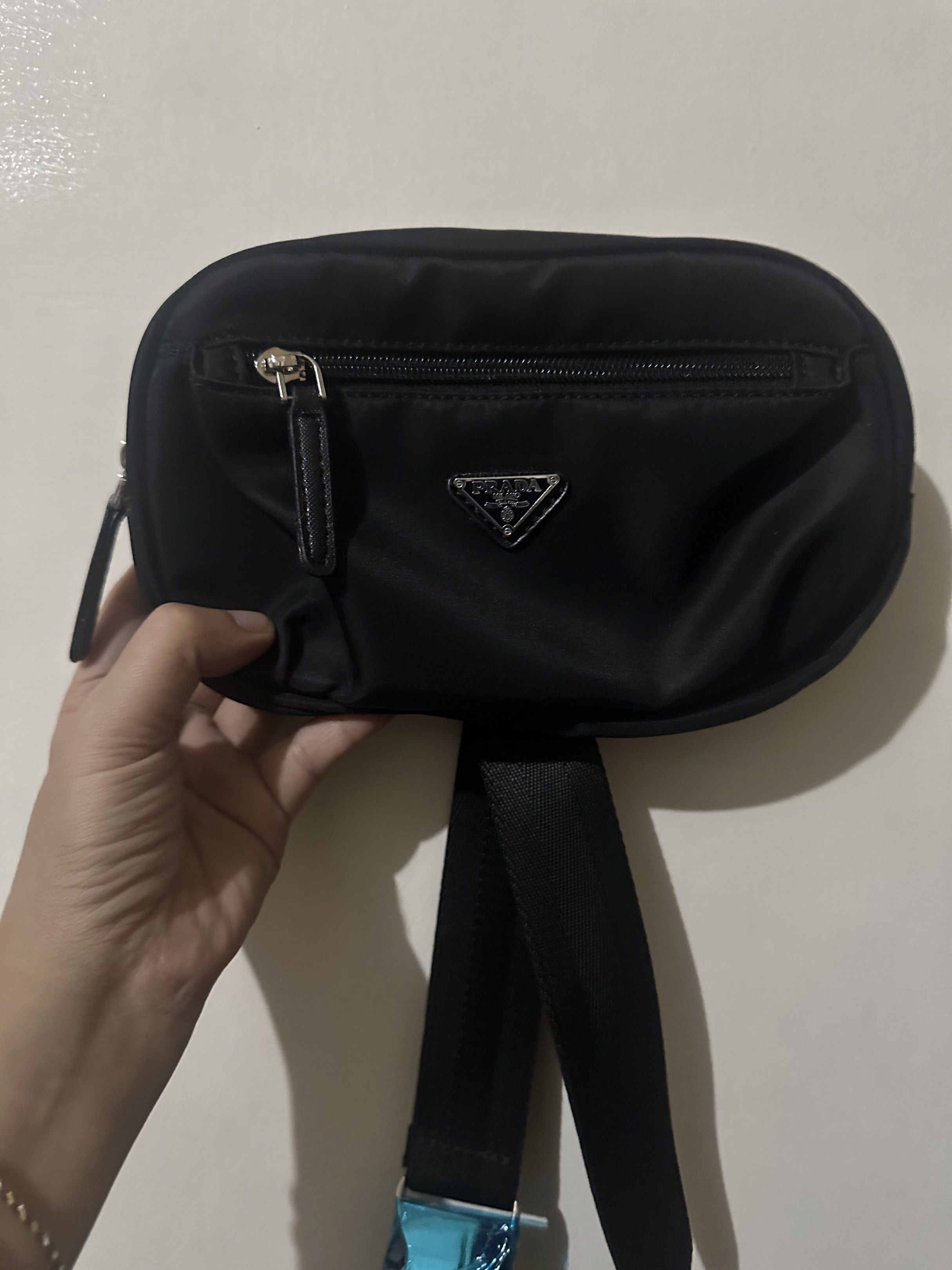 Prada Black Waist Bag (Category: Luxury Bags & Wallets) located in Quezon City. Submitted by biancabubbles8888888 (Listing ID 1418975336, Image 1). Description: Black Prada waist bag. Features a main compartment with a zipper closure and a smaller front pocket. Includes an adjustable black strap with a blue buckle. The Prada logo is visible on the front. Perfect for carrying essentials..