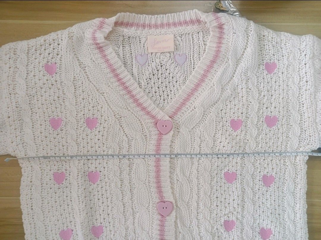 Taylor Swift Lover Cardigan (Category: Coats, Jackets and Outerwear) located in Manila. Submitted by dapperanddazzle (Listing ID 1418872699, Image 2). Description: 🫶🏻 DUPÊ PO ITO, WALANG ORIG NA BELOW 1K ANG PRICE 🫶🏻 hihihi Pre-loved but in perfectly good condition Worn only twice Size: M/L Rfs : Maluwag saken - Cream-colored cardigan - Pink heart details - V-neck design with pink trim - Heart-shaped buttons - Features the words "the Lover" -