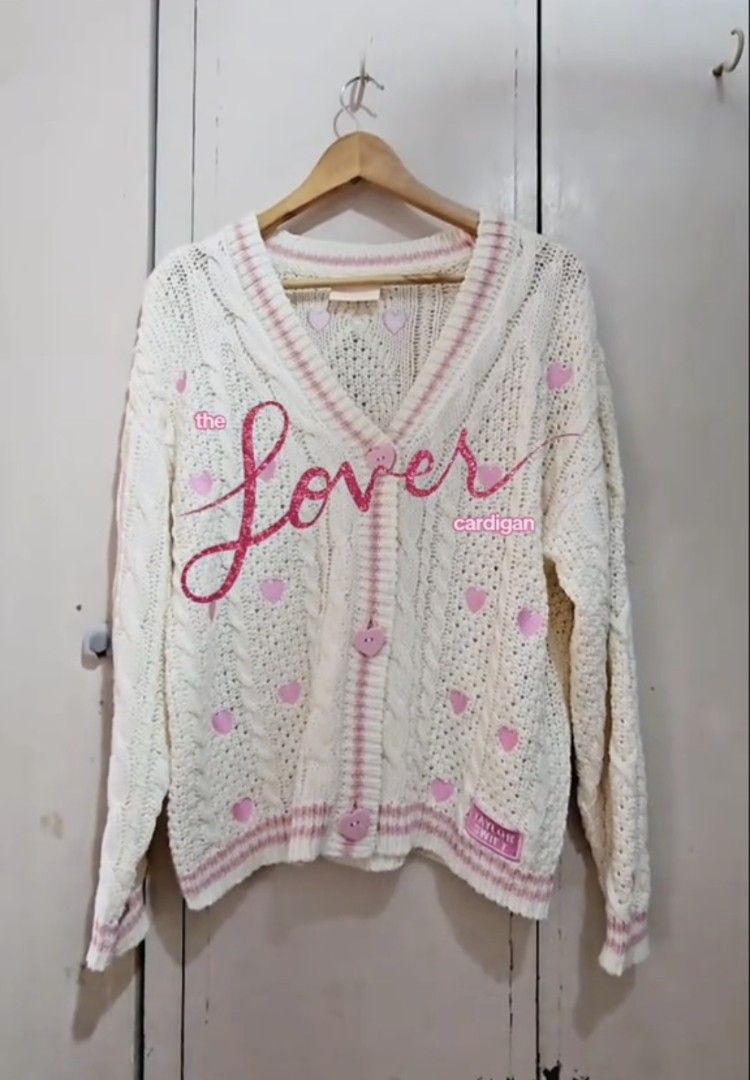 Taylor Swift Lover Cardigan (Category: Coats, Jackets and Outerwear) located in Manila. Submitted by dapperanddazzle (Listing ID 1418872699, Image 1). Description: 🫶🏻 DUPÊ PO ITO, WALANG ORIG NA BELOW 1K ANG PRICE 🫶🏻 hihihi Pre-loved but in perfectly good condition Worn only twice Size: M/L Rfs : Maluwag saken - Cream-colored cardigan - Pink heart details - V-neck design with pink trim - Heart-shaped buttons - Features the words "the Lover" -