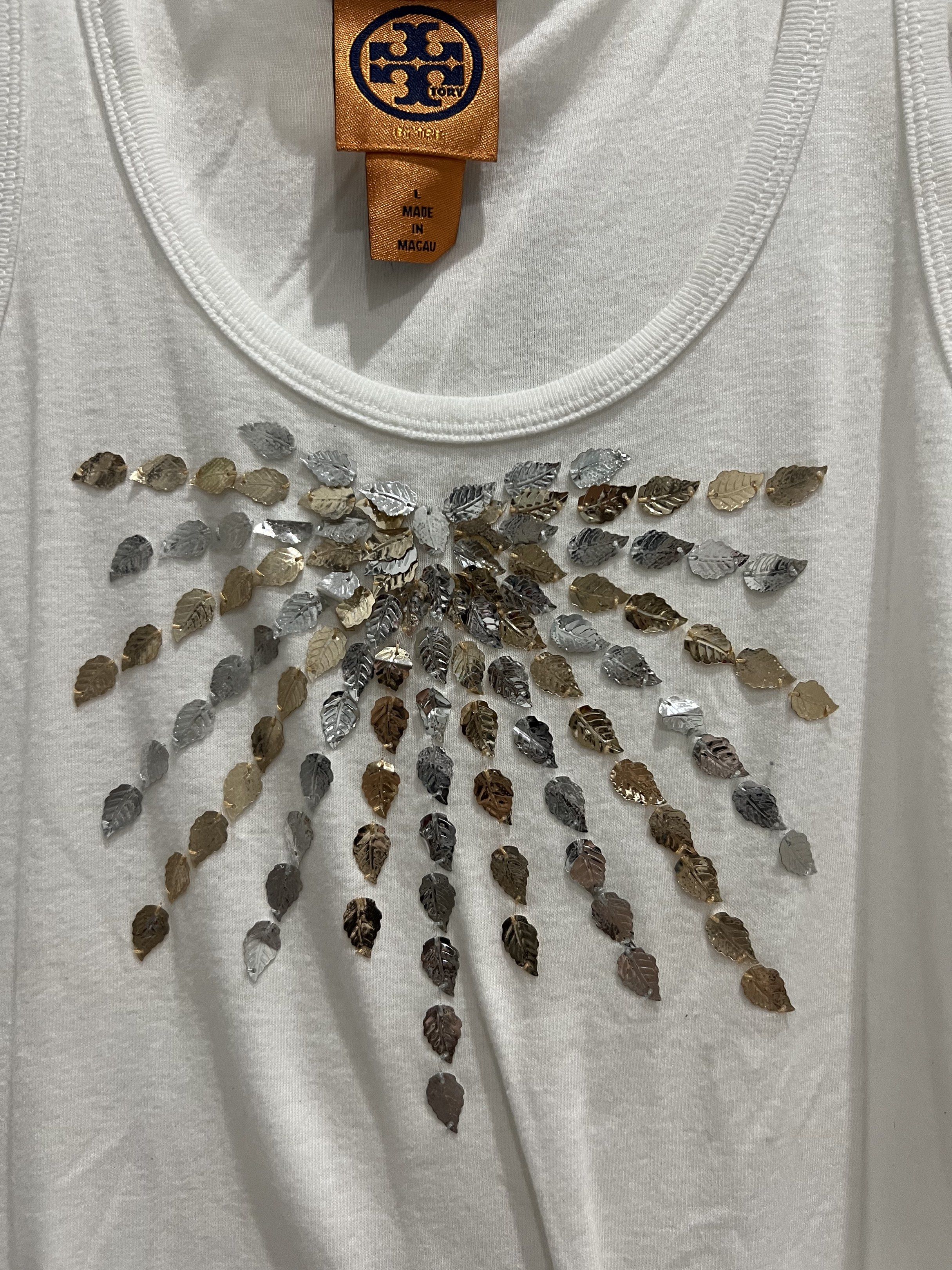 Tory Burch Embellished Tank Top - Size L (Category: Sleeveless) located in Cainta. Submitted by cendzz (Listing ID 1418876480, Image 3). Description: - Tory Burch tank top - White color - M built - Scoop neck, sleeveless design - Leaf-shaped embellishments - Sunburst pattern on chest - Soft, comfortable material.