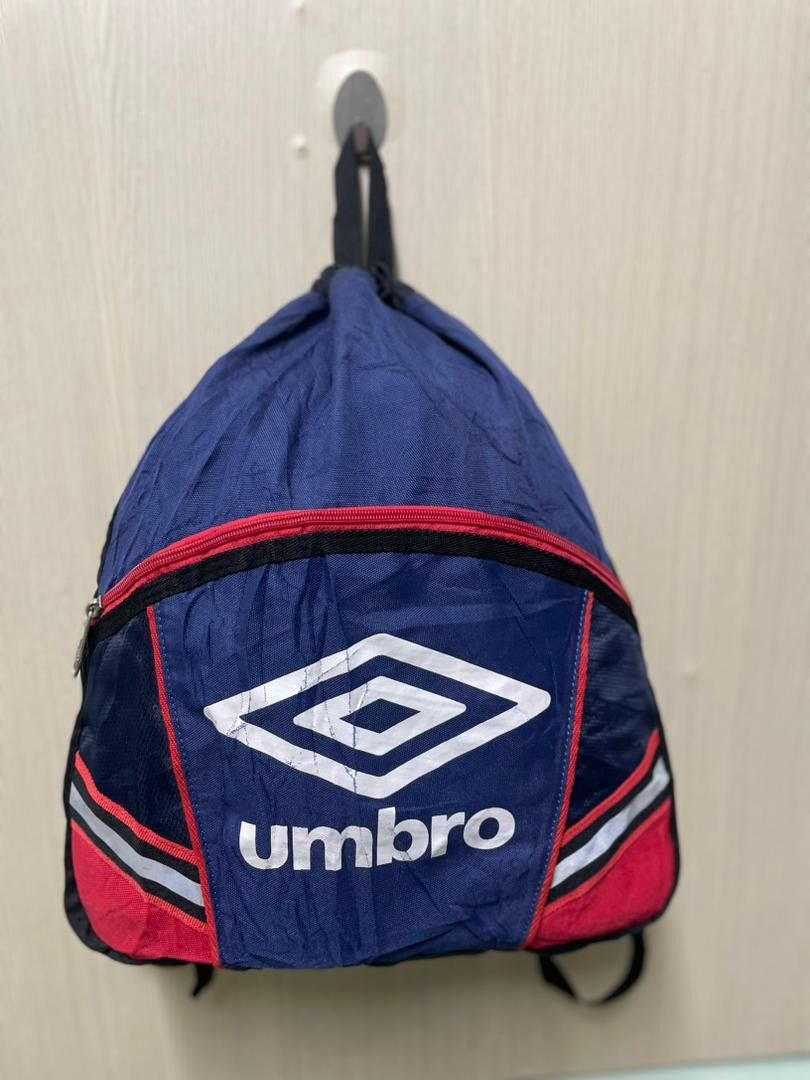 Umbro Drawstring Backpack (Category: Backpacks) located in Tanah Merah. Submitted by fiz_wa88 (Listing ID 1418944833, Image 1). Description: - Umbro drawstring backpack - Color: Navy blue, red, and black - Features Umbro logo - Includes a zipper pocket - Adjustable straps - Model number: A1678J - Material: Nylon.