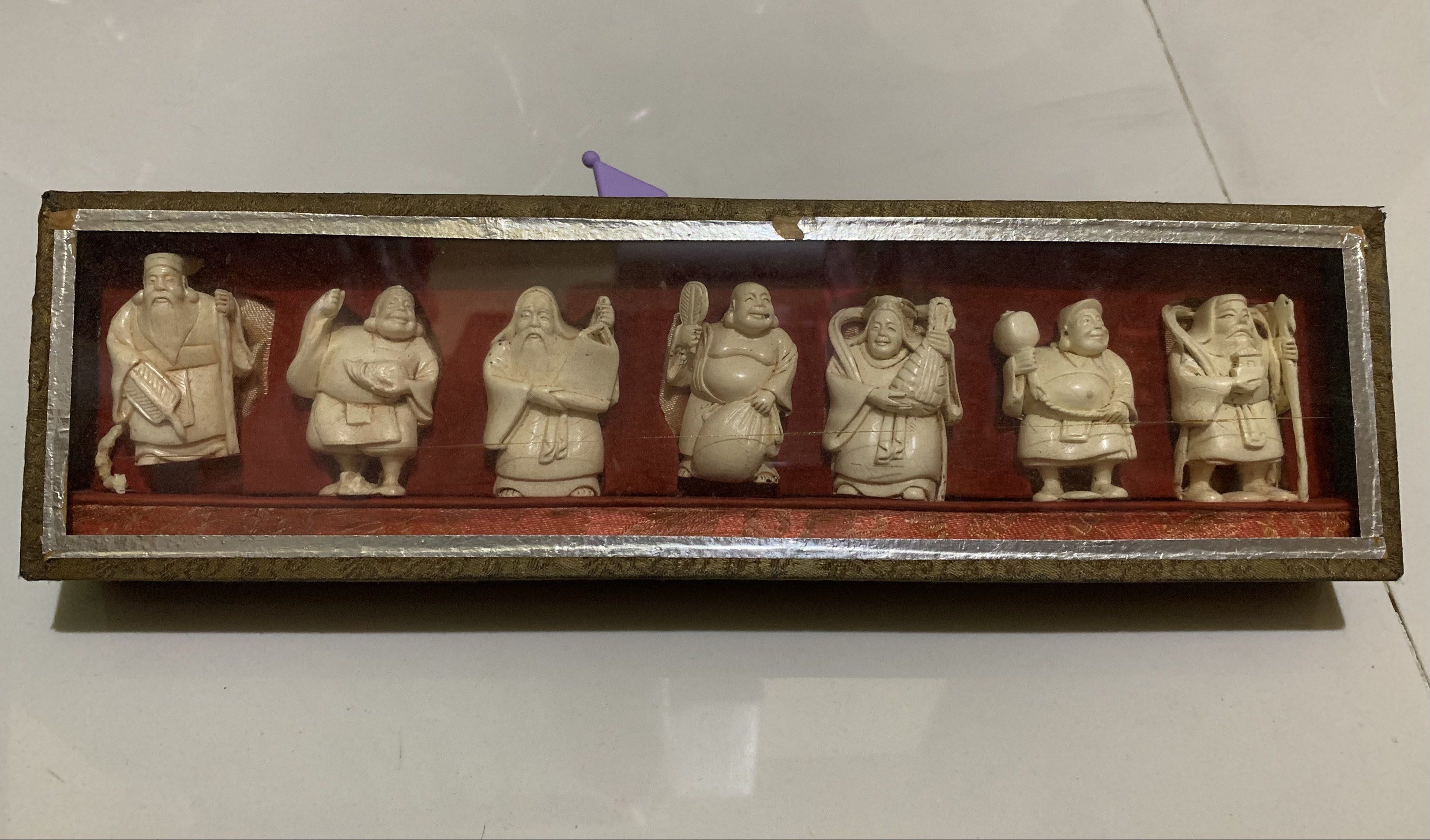 Vintage Seven Lucky Gods Figurines Set (Category: Vintage Collectibles) located in Quezon City. Submitted by ncjnc (Listing ID 1418924584, Image 2). Description: - Set of seven figurines representing the Seven Lucky Gods. - Presented in a rectangular box with a clear lid. - Figurines are carved in a light color (ivory-like). - Each figure has a unique pose and accessories. - Box features a red interior and decorative border..