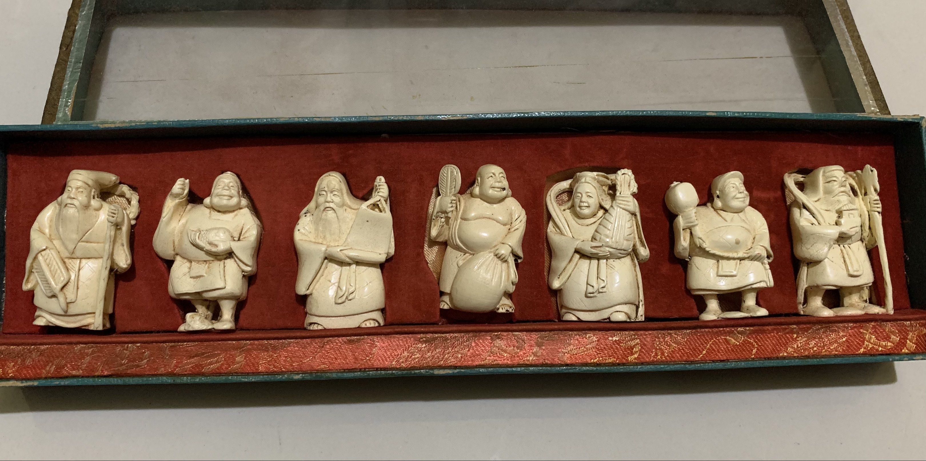 Vintage Seven Lucky Gods Figurines Set (Category: Vintage Collectibles) located in Quezon City. Submitted by ncjnc (Listing ID 1418924584, Image 3). Description: - Set of seven figurines representing the Seven Lucky Gods. - Presented in a rectangular box with a clear lid. - Figurines are carved in a light color (ivory-like). - Each figure has a unique pose and accessories. - Box features a red interior and decorative border..