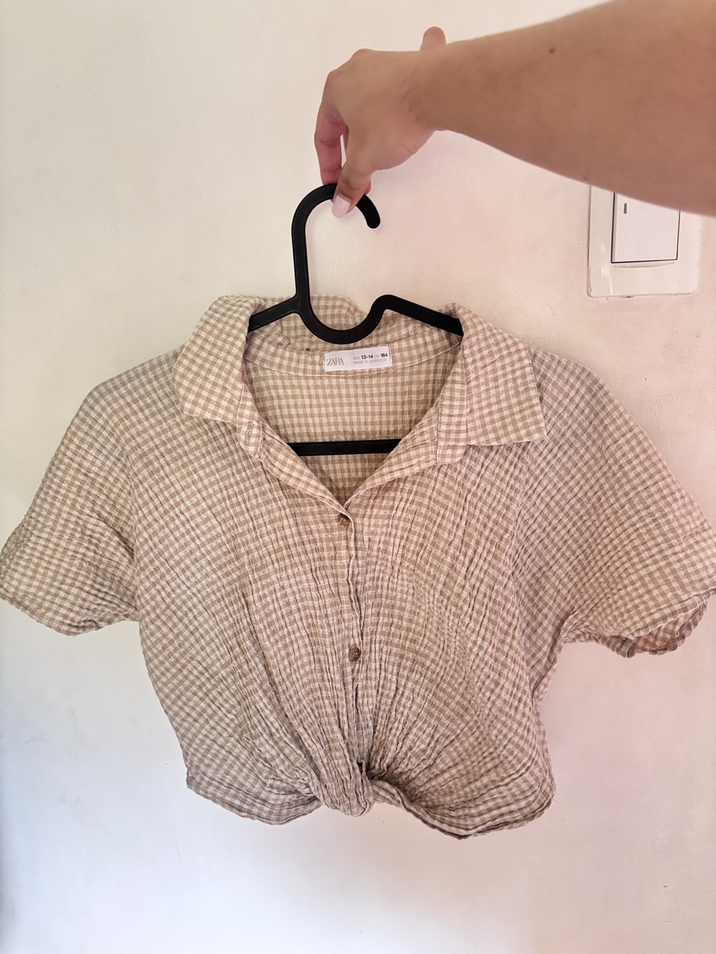 Zara Gingham Crop Top (Category: Sleeveless) located in Meycauayan. Submitted by declutter0403 (Listing ID 1418816275, Image 1). Description: - Zara crop top - Gingham pattern - Color: Beige and brown - Features: Collared neckline, short sleeves, knotted front - Closure: Button-down - Size: Not specified.